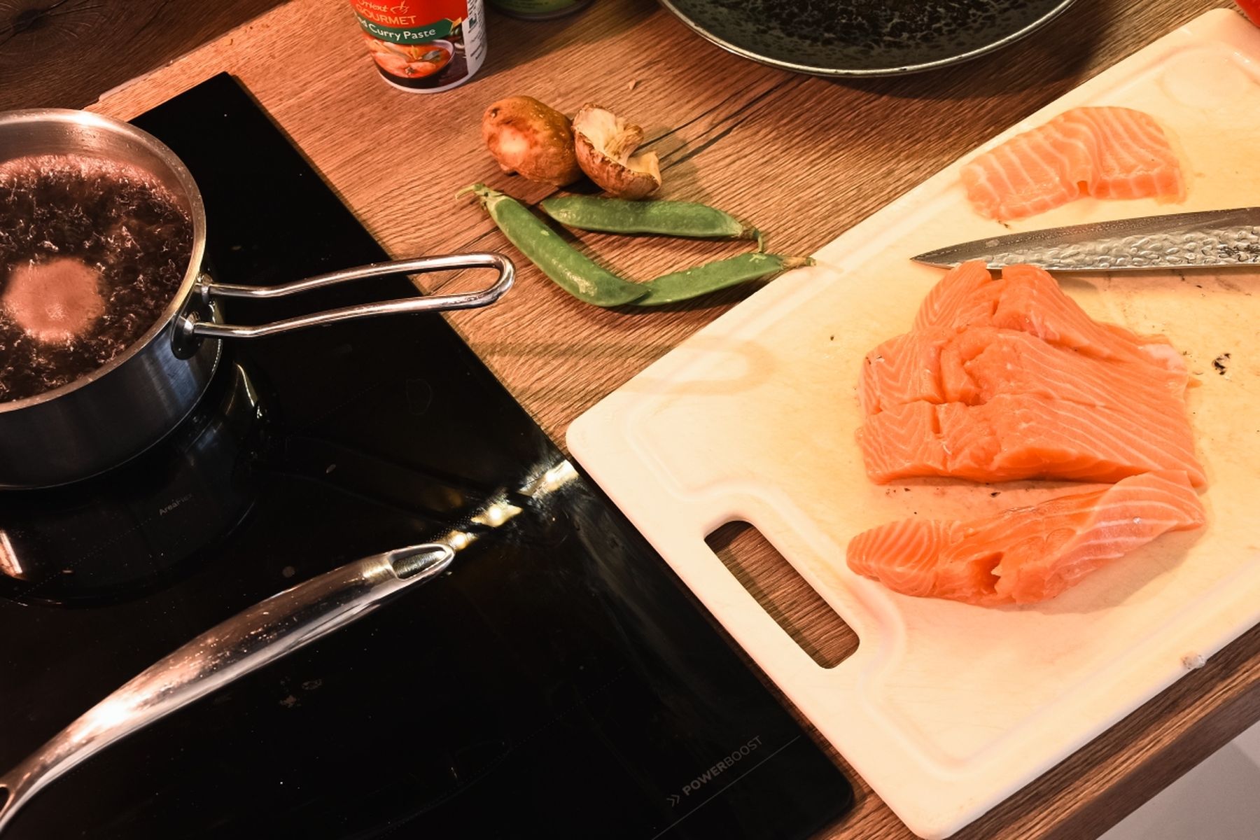 Filety z lososa a nůž na prkénku, vedle hrášek, žampiony a kari pasta, na sporáku se vaří v rendlíku černá rýže. Recept připravil Vojta Poštulka.