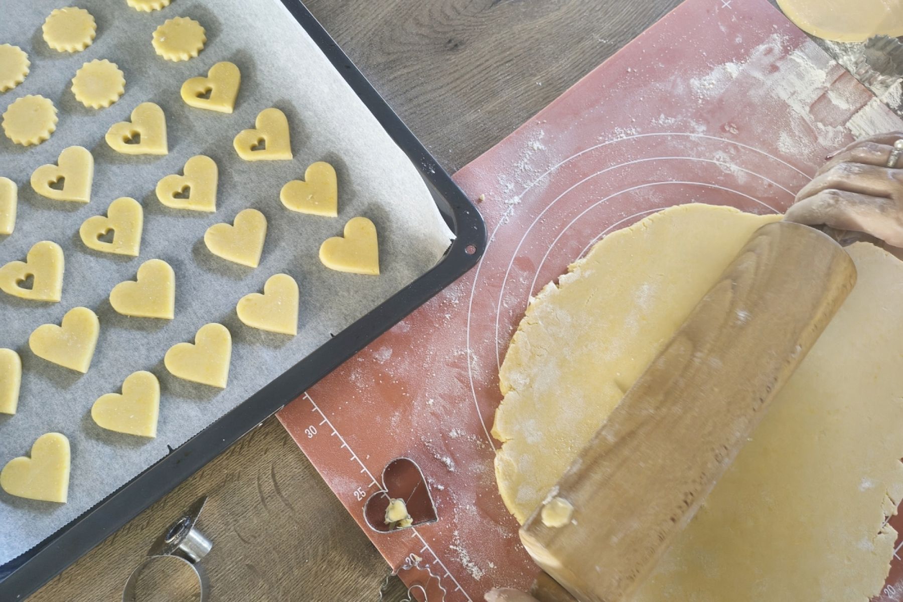Srdíčkové a kulaté linecké cukroví na plechu, vedle rozválené těsto na pomoučené pracovní ploše, ze kterého se vykrajují další tvary. Recept připravily Ségry v kuchyni.
