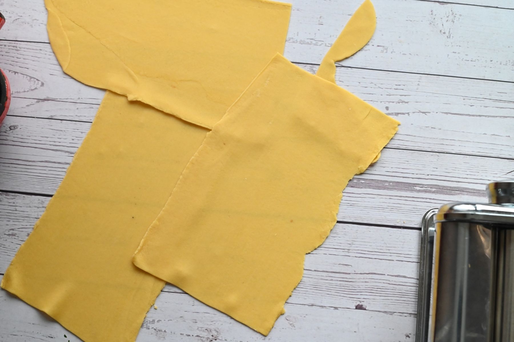 Pláty čerstvého těsta na těstoviny na bílém dřevěném povrchu vedle strojku na těstoviny. Recept připravil Vojta Poštulka.