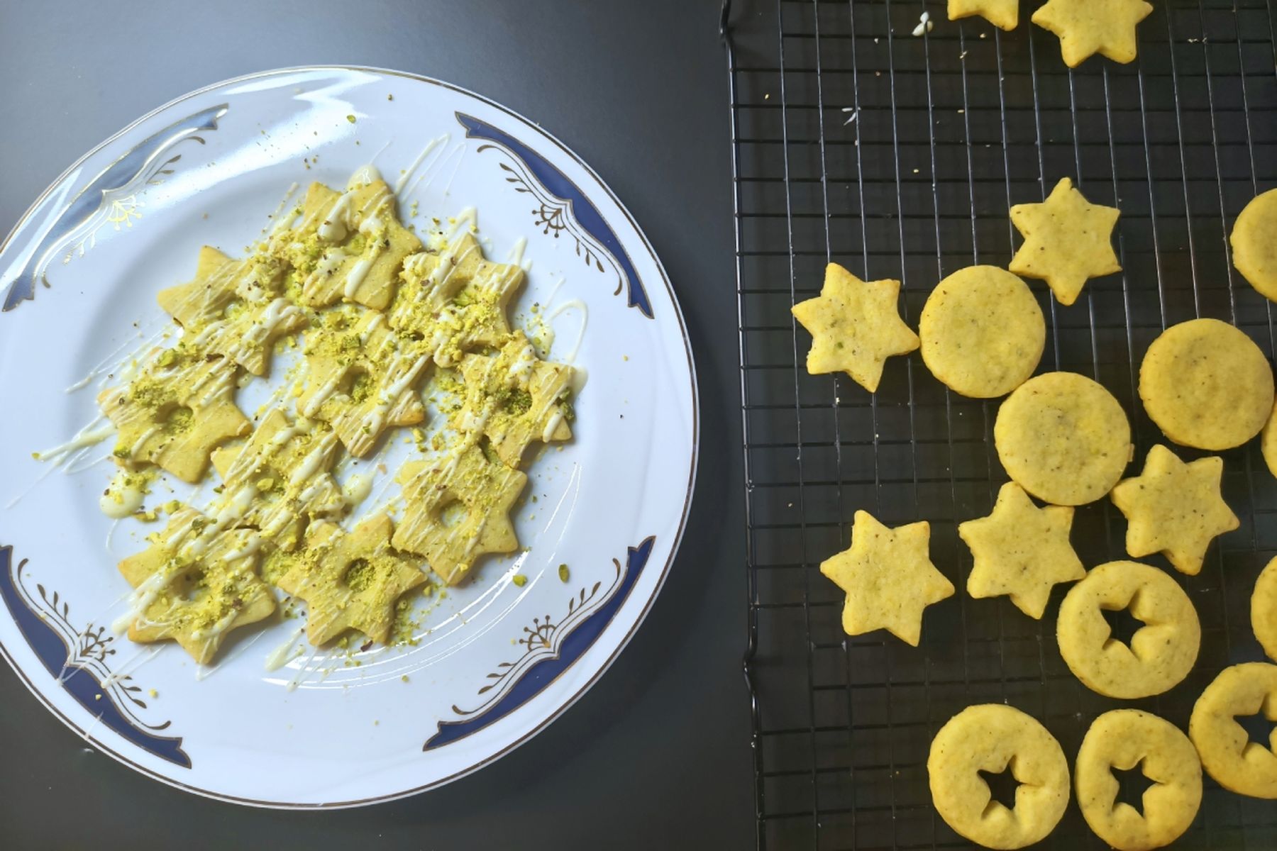 Hvězdičkové a kulaté cukroví na chladicí mřížce, část polévaná bílou čokoládou a posypaná pistáciemi na ozdobném talíři. Recept připravily Ségry v kuchyni.
