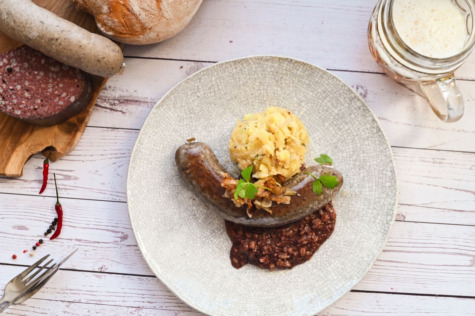 Talíř s jitrnicí s prejtem, bramborovou kaší a ozdobou. V pozadí chléb a pivo na dřevěném stole.