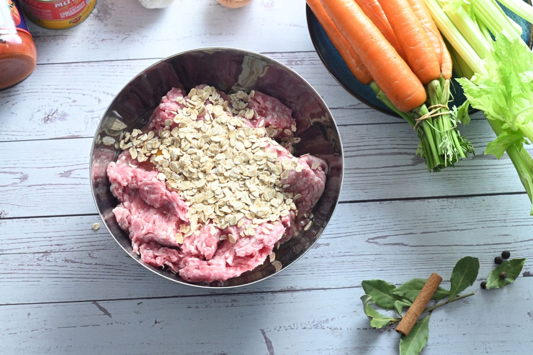 Mísa s mletým masem a ovesnými vločkami, kolem mrkev, řapíkatý celer a koření na dřevěném povrchu. Recept připravil Vojta Poštulka.