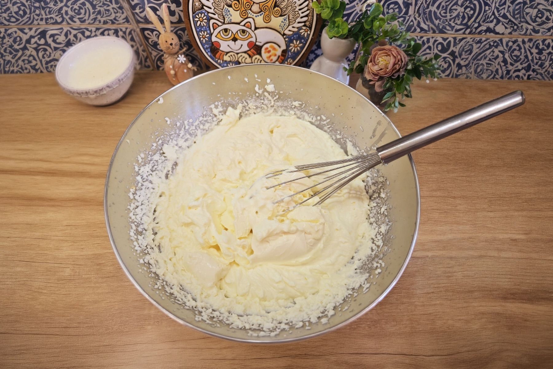 Mísa s krémem, který je šlehán metličkou na dřevěné pracovní desce, kolem keramické dekorace a malá rostlina. Recept připravil Táta v akci.