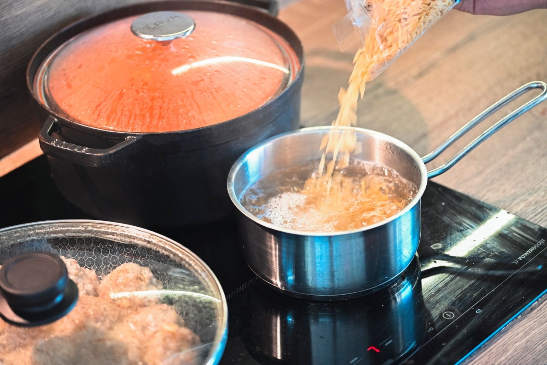 Těstovinová rýže sypaná do hrnce s vroucí vodou na sporáku, v pozadí hrnce. Recept připravil Vojta Poštulka.