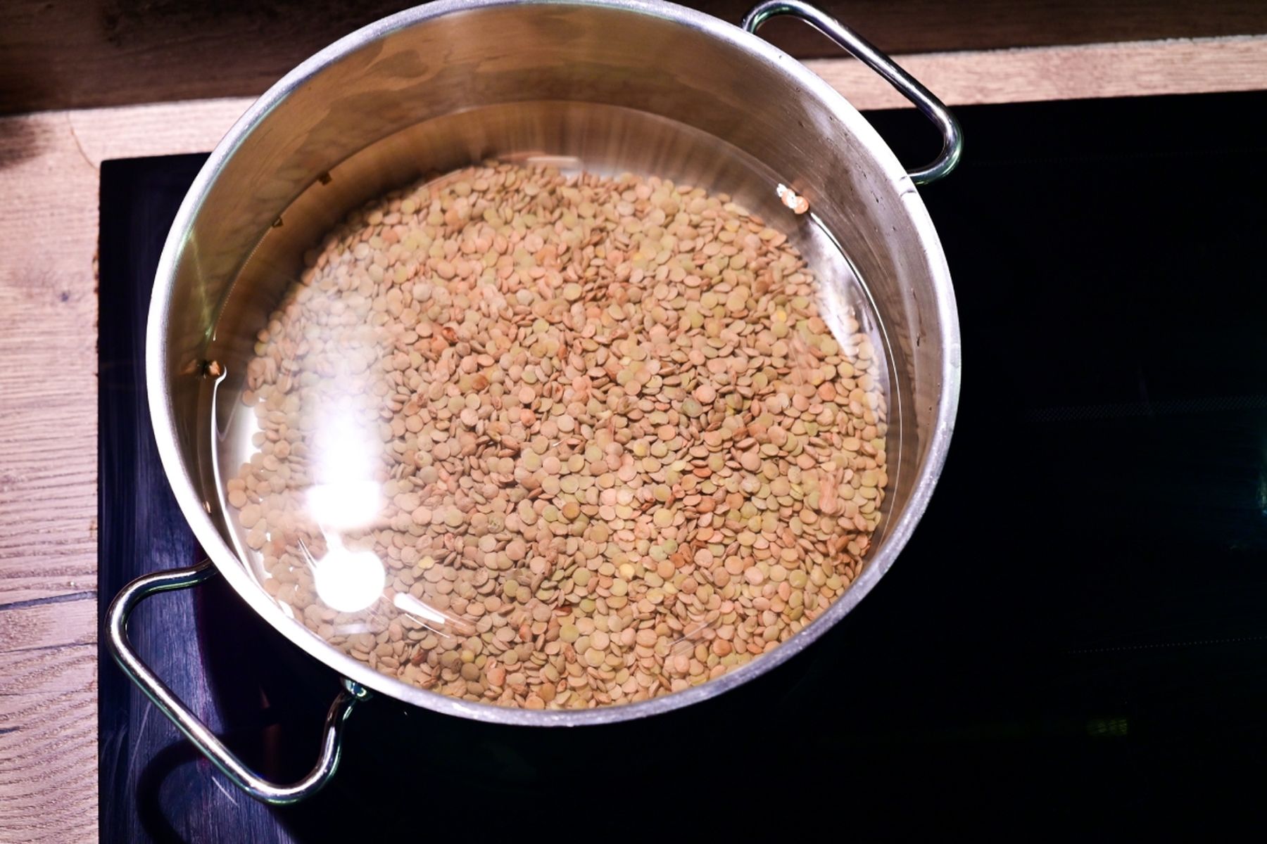 Nerezový hrnec s hnědou čočkou namočenou ve vodě postavený na černé varné desce. Recept je z nabídky Globus a připravil ho Vojta Poštulka.