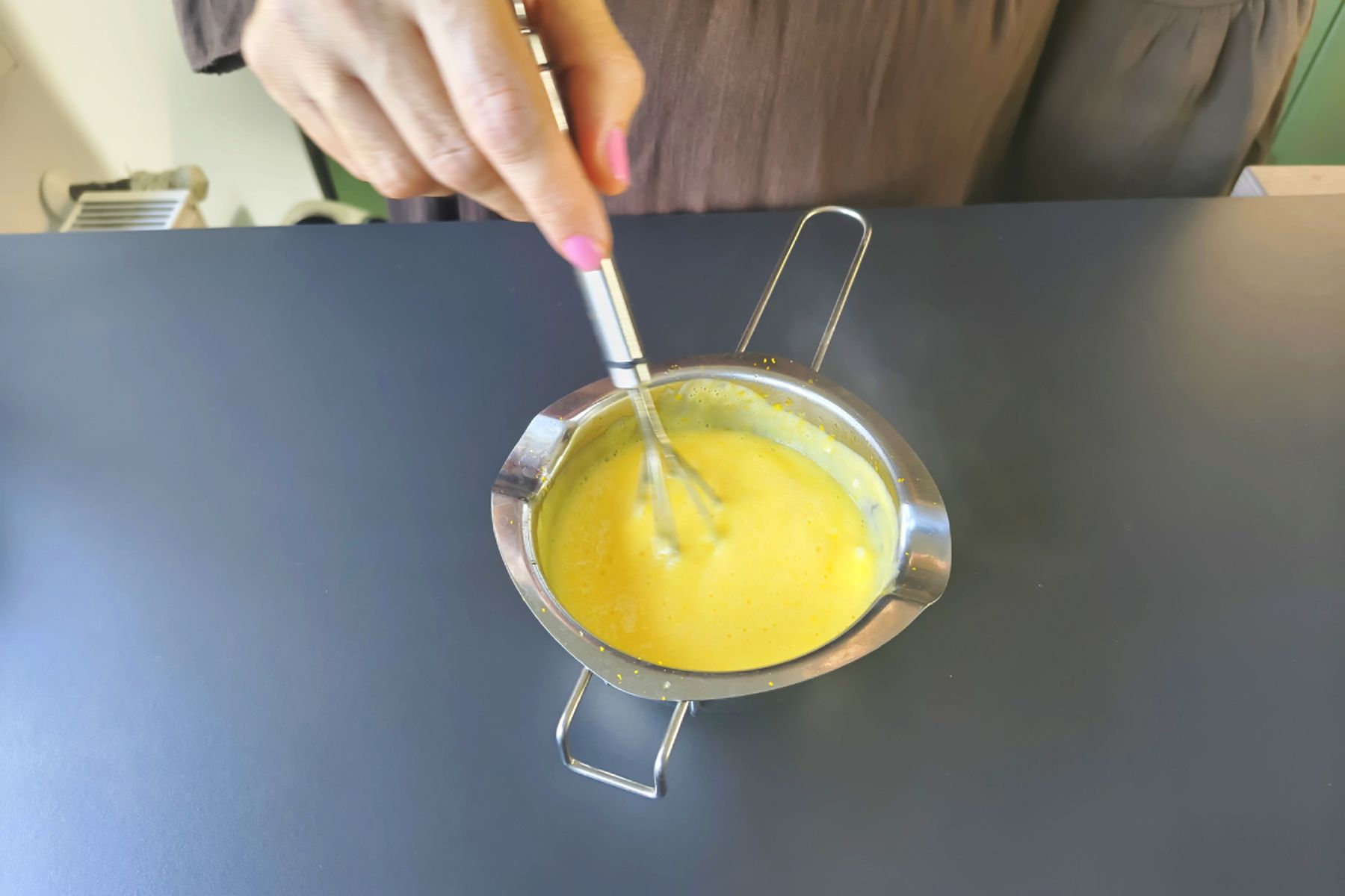 Osoba šlehá metličkou pomerančový curd v kovové míse na tmavé pracovní ploše. Recept připravily Ségry v kuchyni.