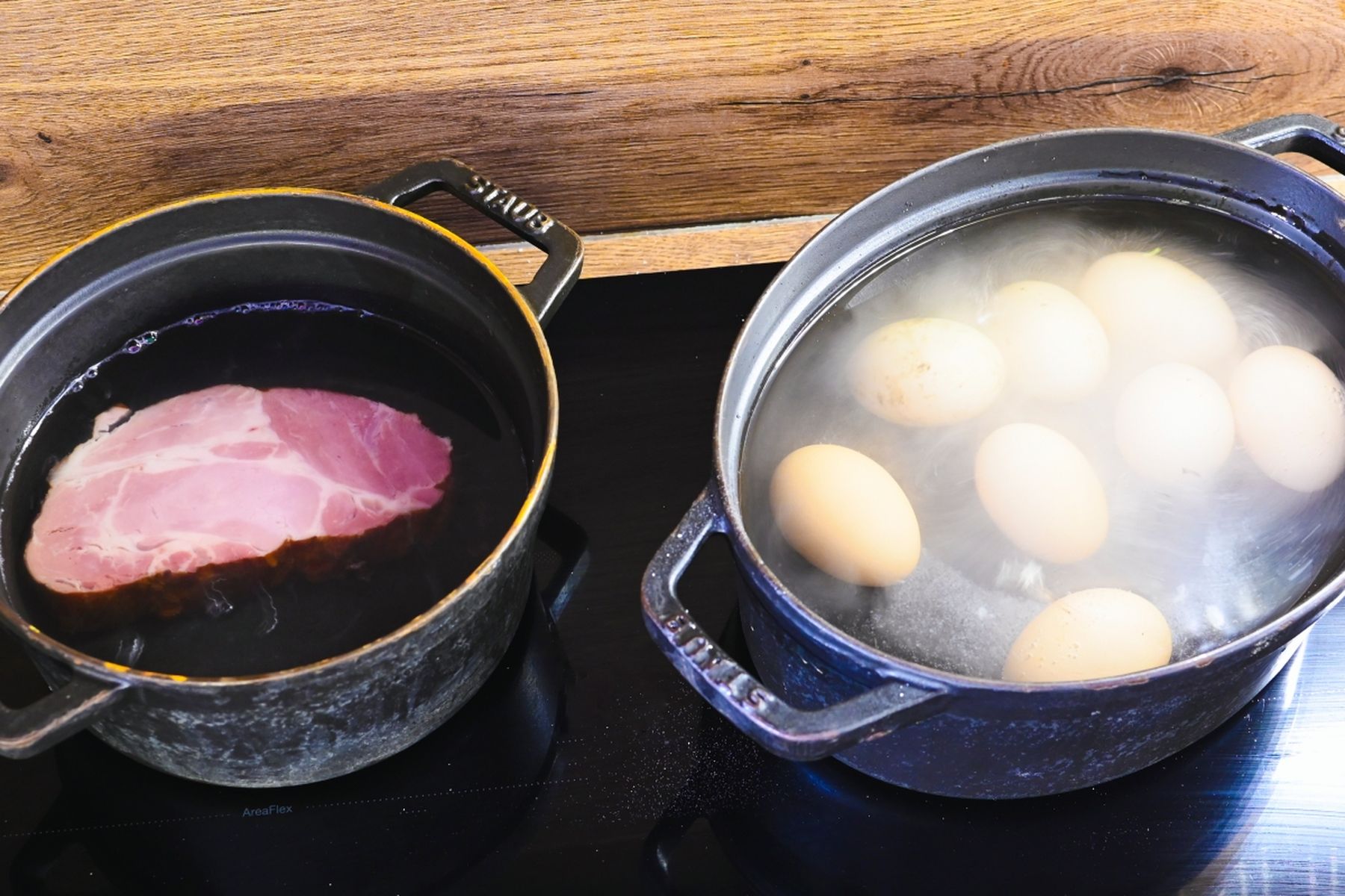 Dva hrnce na sporáku – v jednom se vaří uzená krkovice, ve druhém se vaří osm vajec. V pozadí dřevěná pracovní deska. Recept připravil Vojta Poštulka.