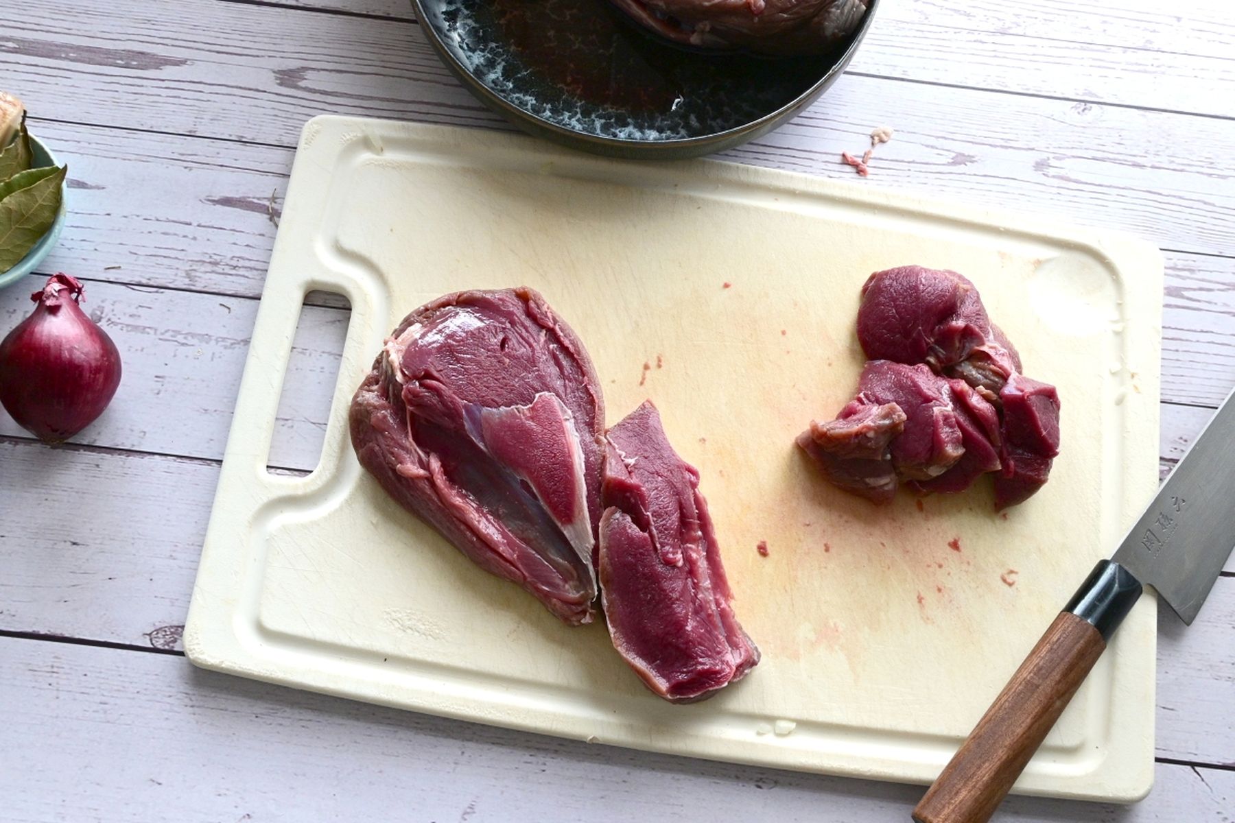 Syrové srnčí maso na prkénku s nožem a červenou cibulí, připravené k vaření, na dřevěném stole. Recept připravil Vojta Poštulka.