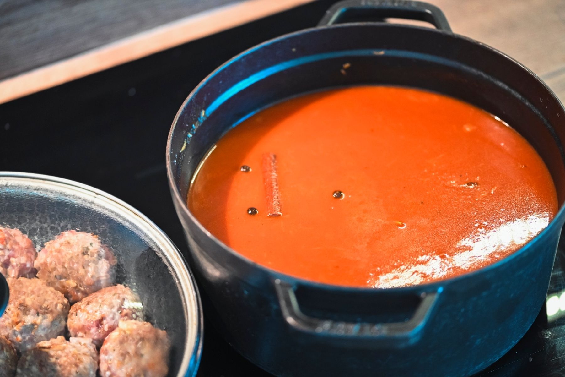 Hrnec s hustou rajčatovou omáčkou se skořicí a kuličkami černého pepře, vedle talíř se syrovými masovými kuličkami. Recept připravil Vojta Poštulka.
