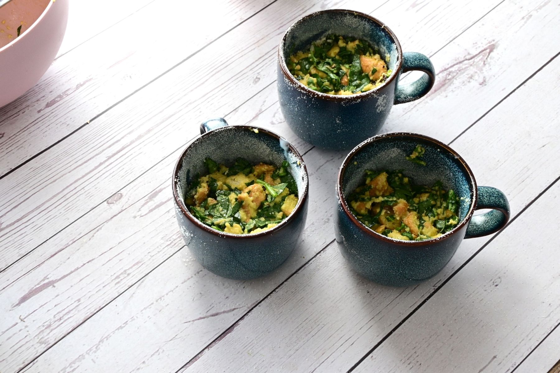 Tři tyrkysové hrnky na bílém dřevěném stole, každý naplněný směsí na špenátový knedlík. Recept připravil Vojta Poštulka..