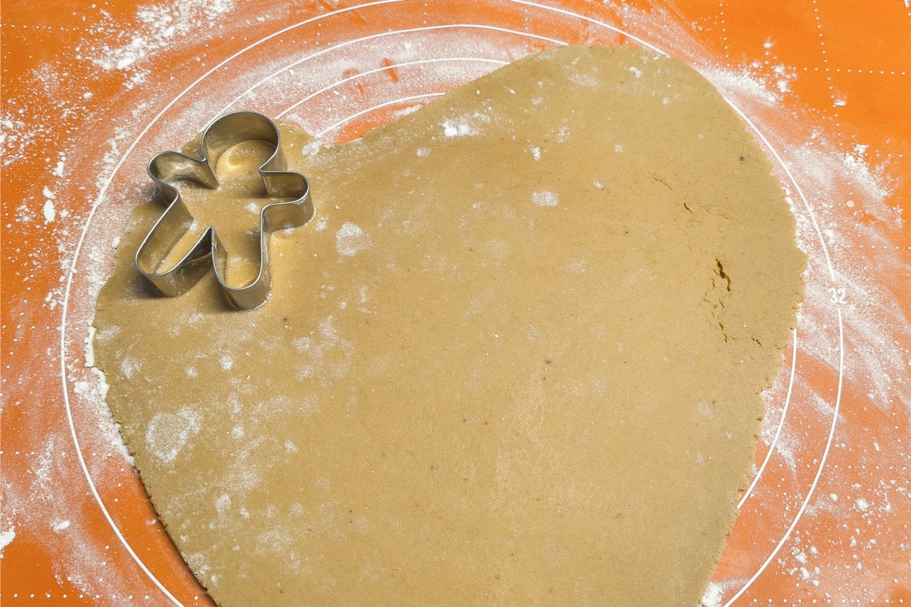 Perníkové těsto na oranžové podložce posypané moukou, do kterého je částečně vtlačená kovová vykrajovací forma ve tvaru perníčku. Recept připravily Ségry v kuchyni.