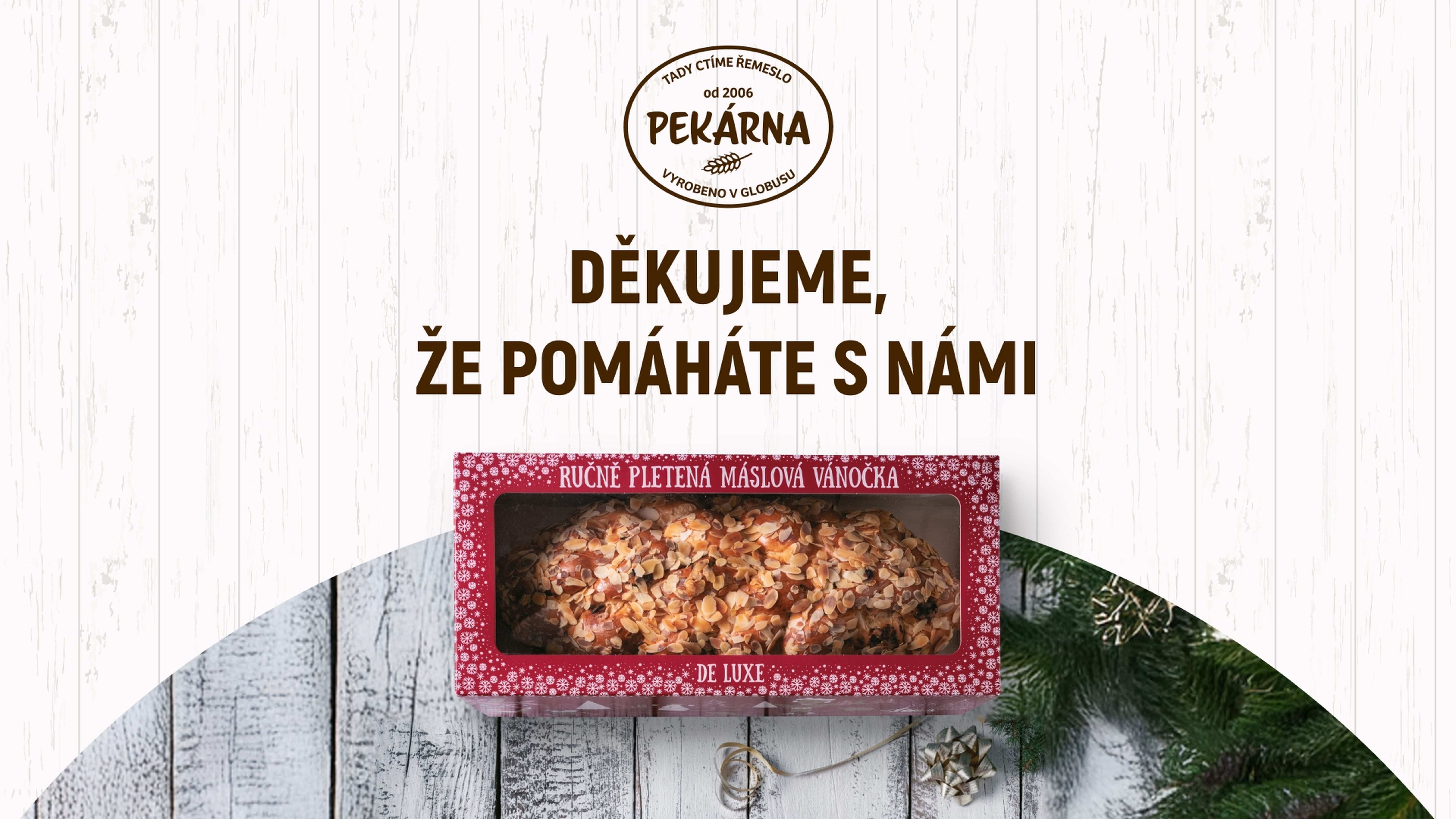 Krabice s kilovou Máslovou vánočkou de luxe na dřevěném stole s vánočními ozdobami; nad ní český text "Děkujeme, že pomáháte s námi" a logo Pekárny Globus.