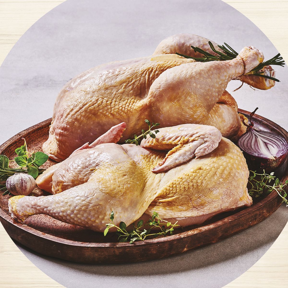 Dvě syrová celá kuřata na dřevěném podnose s bylinkami, cibulí a česnekem, obklopená ilustracemi kuřete na dřevěném pozadí.