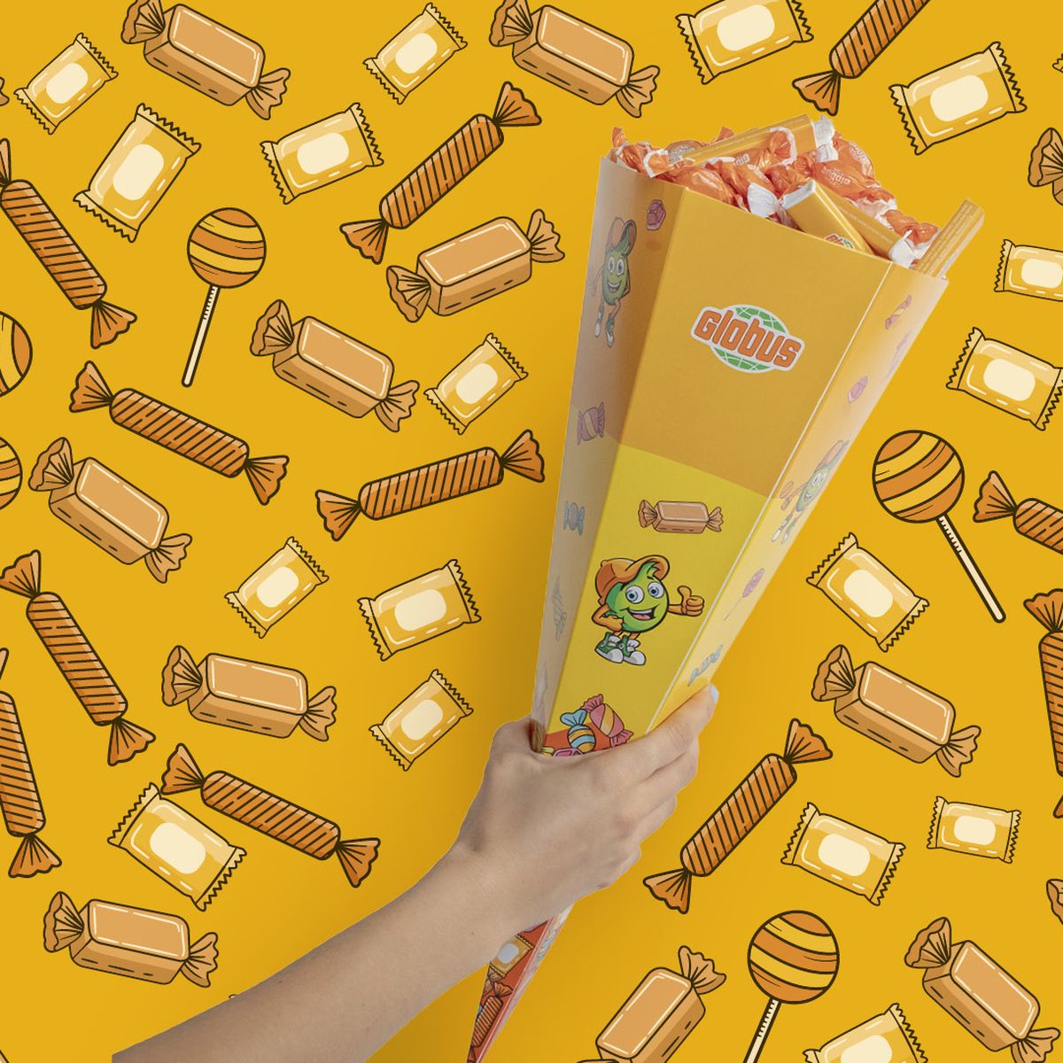 Ruka drží bonboniéru na zářivě oranžovém pozadí plném různých ilustrací bonbónů.