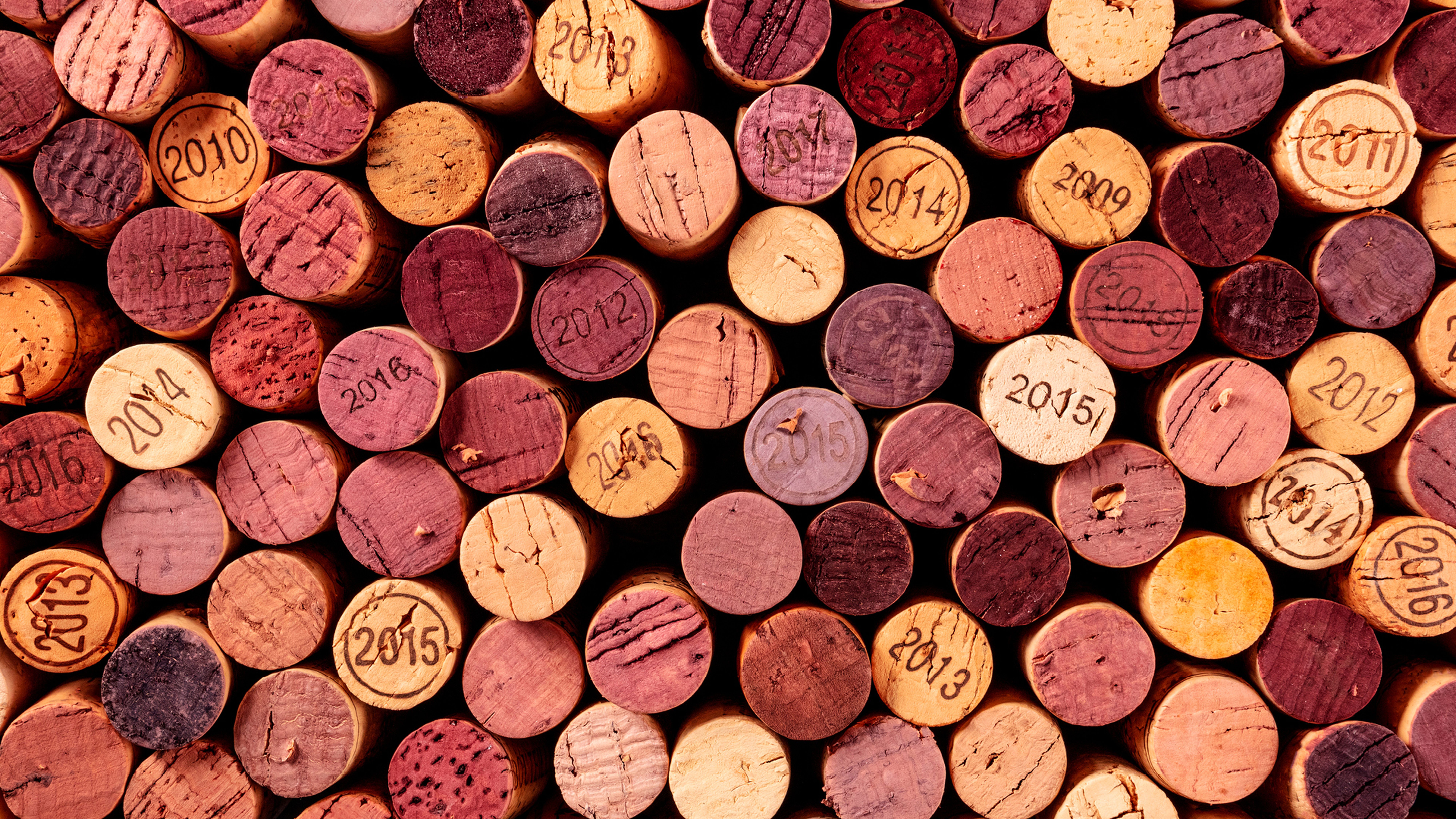 Kolekce zátek na víno uspořádaných vedle sebe, zobrazující různé ročníky od roku 2009 do roku 2016, v odstínech červené, růžové a béžové.