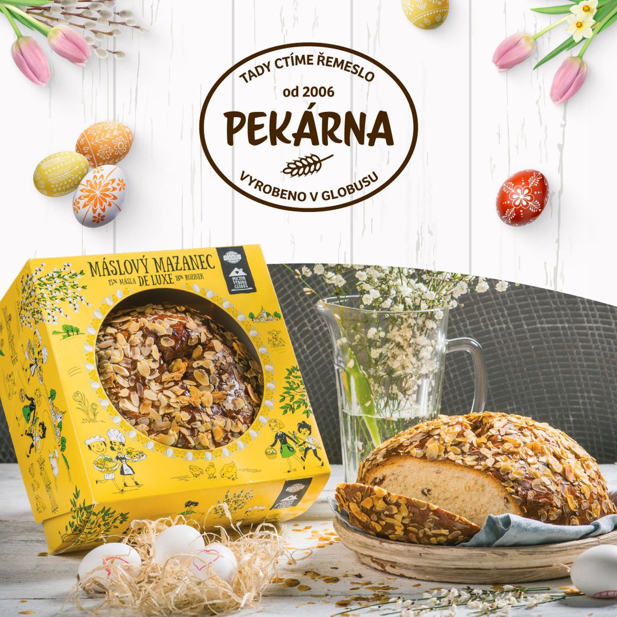 Velikonoční mazanec z Vlastních výrob Globus v krabici a na stole, obklopený velikonoční výzdobou a květinami, pod nápisem Pekárna Globus.
