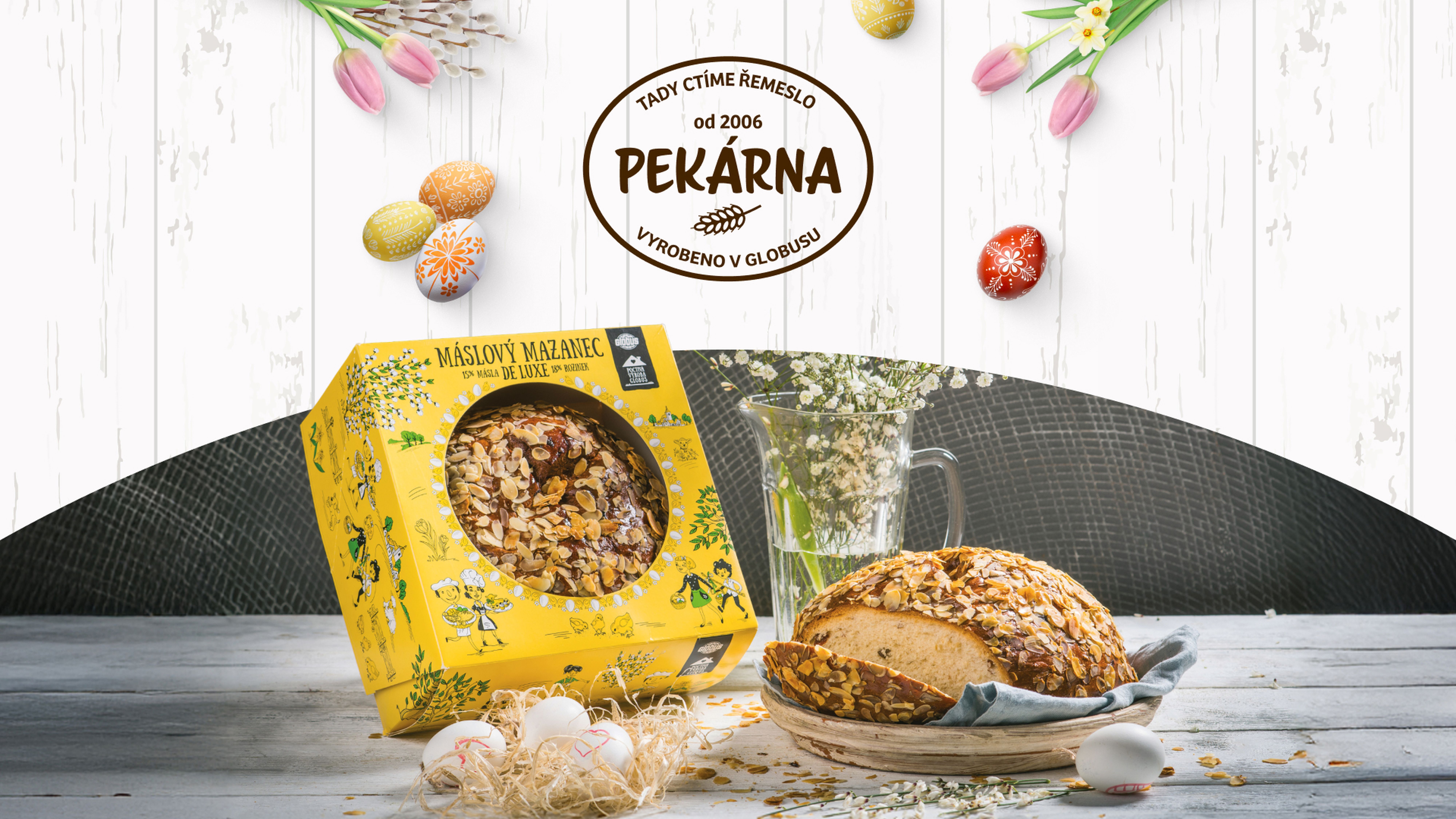 Velikonoční mazanec z Vlastních výrob Globus v krabici a na stole, obklopený velikonoční výzdobou a květinami, pod nápisem Pekárna Globus.