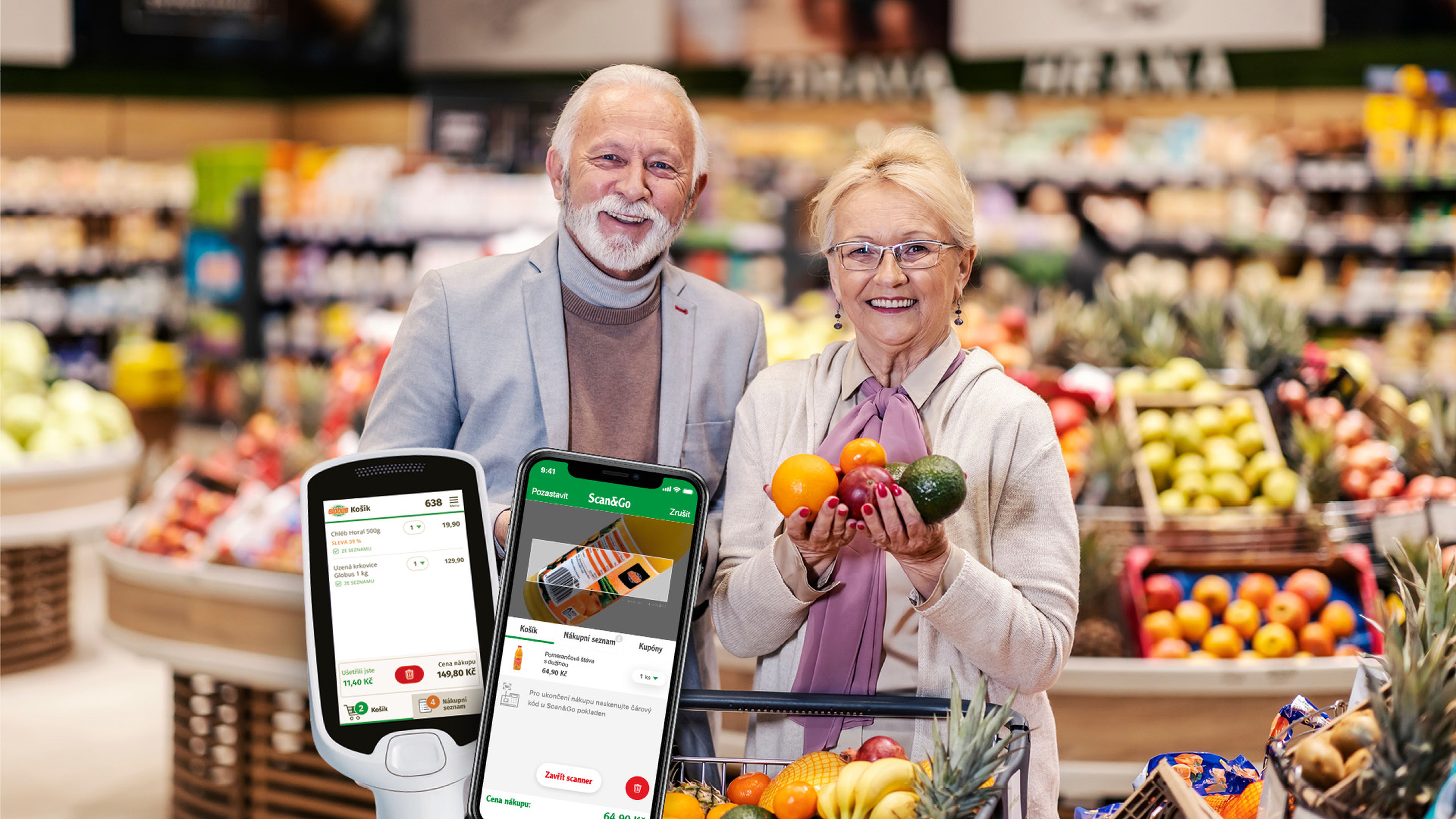 Starší pár s úsměvem při nakupování v hypermarketu, držící různé ovoce. V popředí jsou vidět chytré telefony s nákupní aplikací.