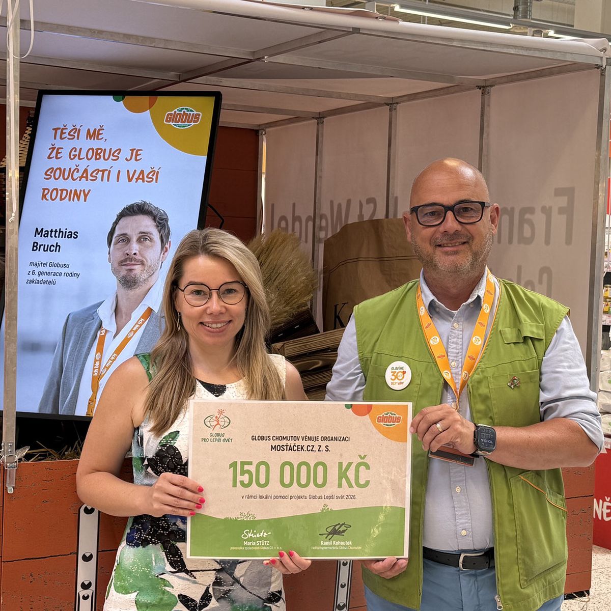 Dvě osoby drží v obchodě velký šek na 150 000 Kč, v pozadí je plakát a potraviny.