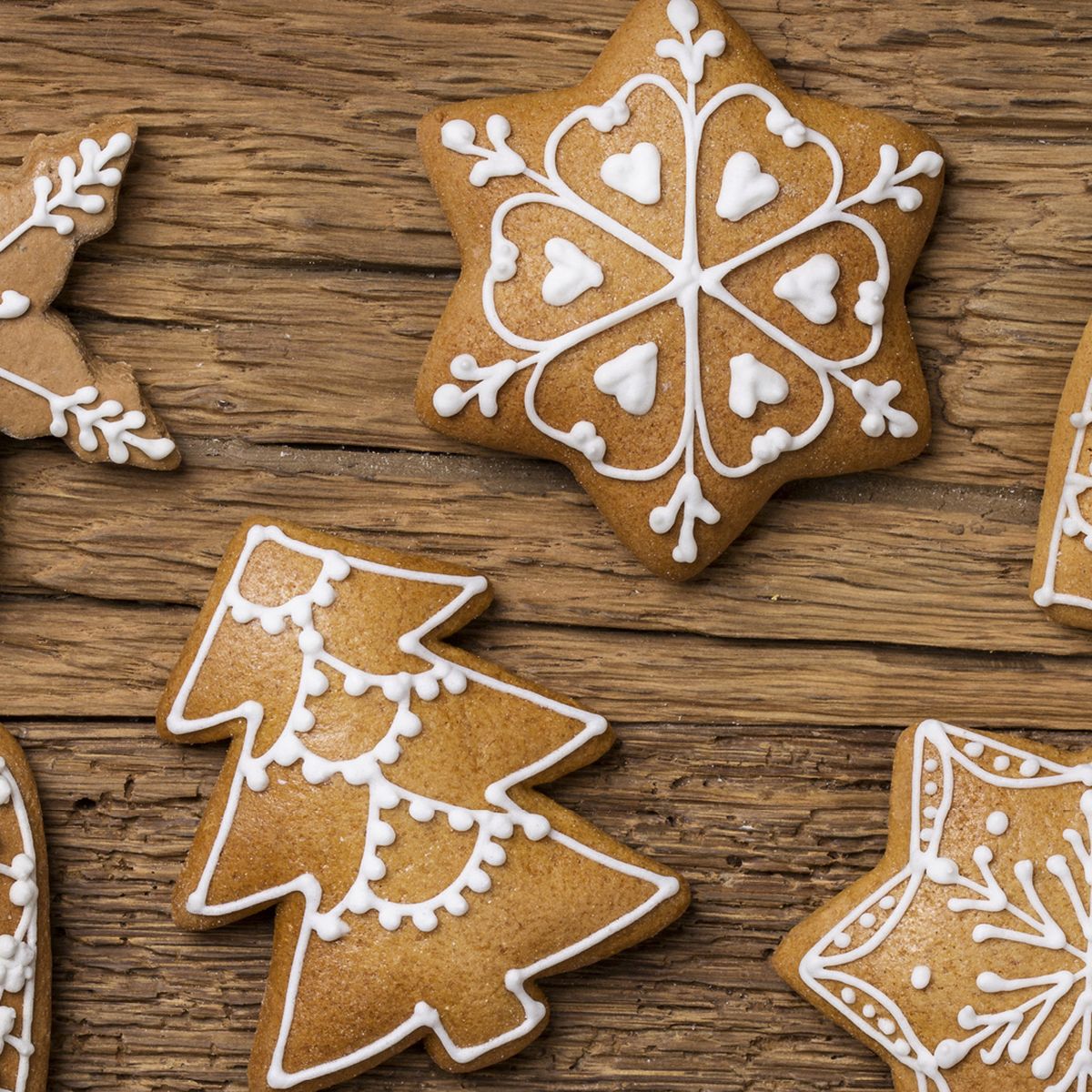 Na hnědém dřevěném podkladu jsou perníčky ve tvaru vločky, hvězdy, srdce a stromečku ozdobené bílou polevou.