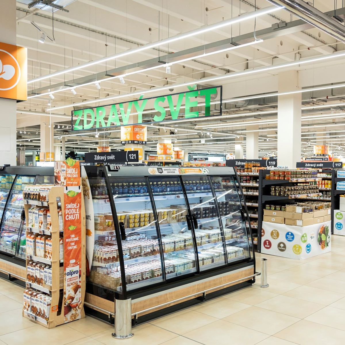 A spacious grocery store aisle with dairy sections on the left and shelves filled with various packaged goods on the right, under bright lighting.