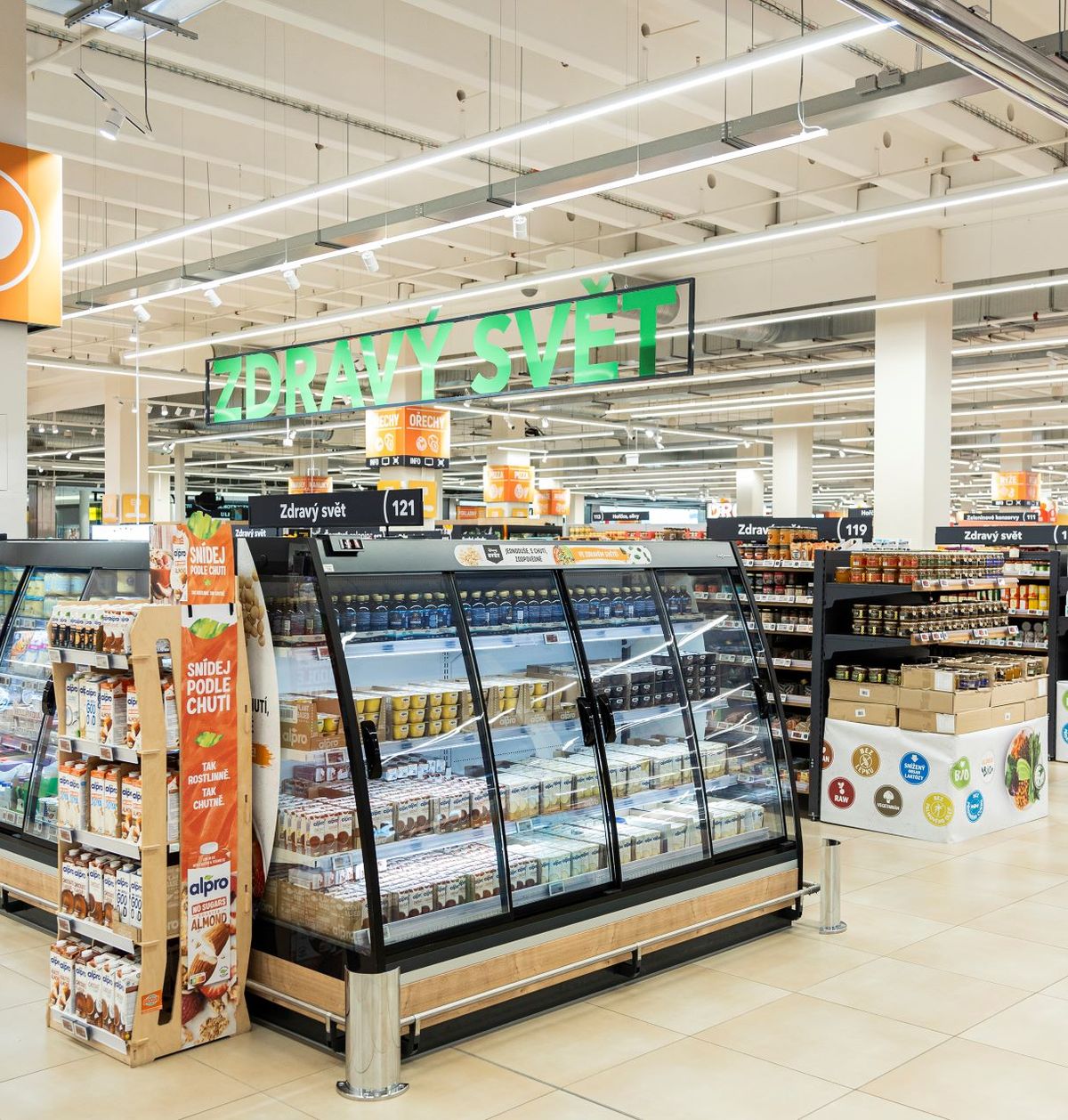 A spacious grocery store aisle with dairy sections on the left and shelves filled with various packaged goods on the right, under bright lighting.