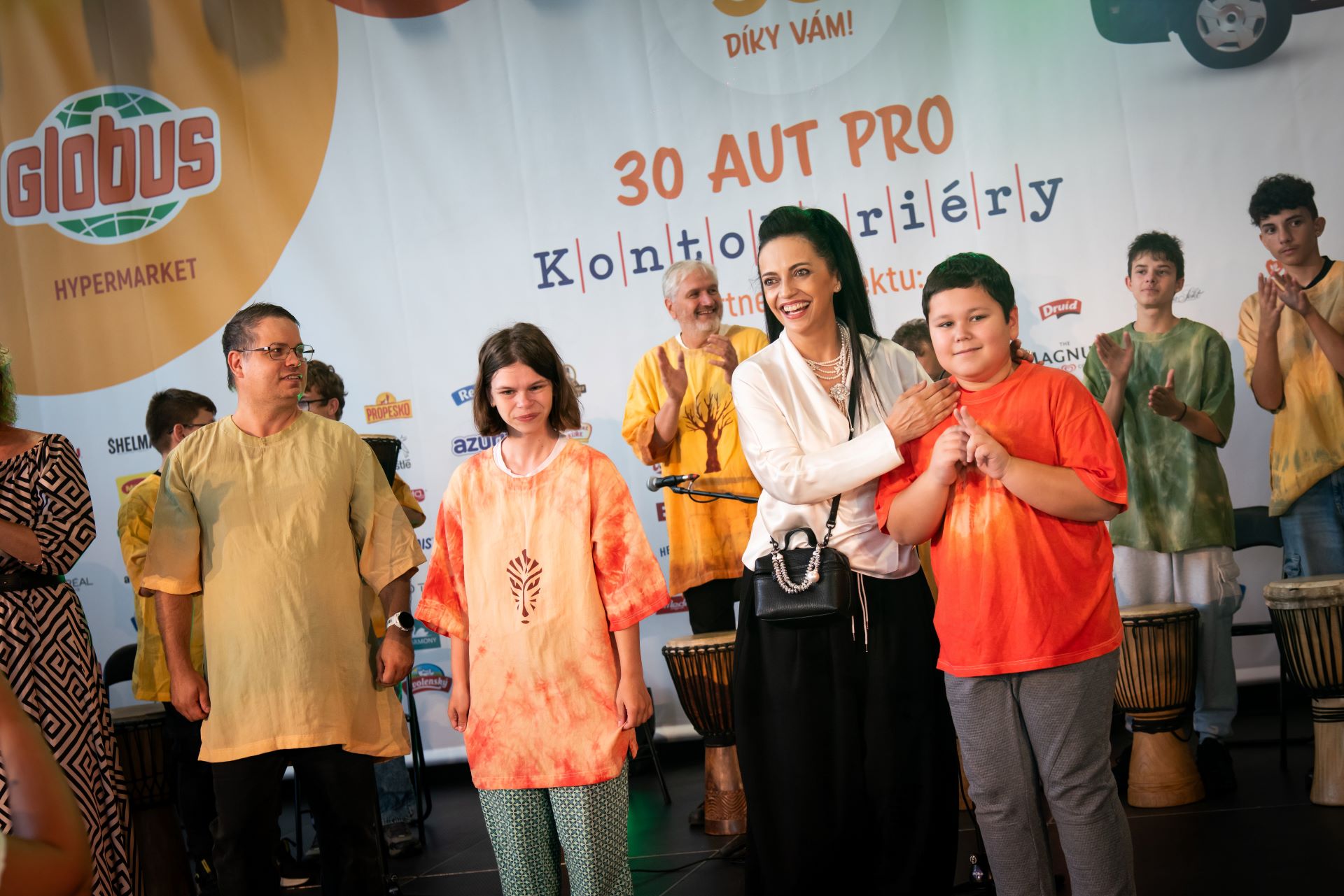 Skupina lidí na pódiu během akce, v pozadí je vidět transparent a všichni tleskají a usmívají se.