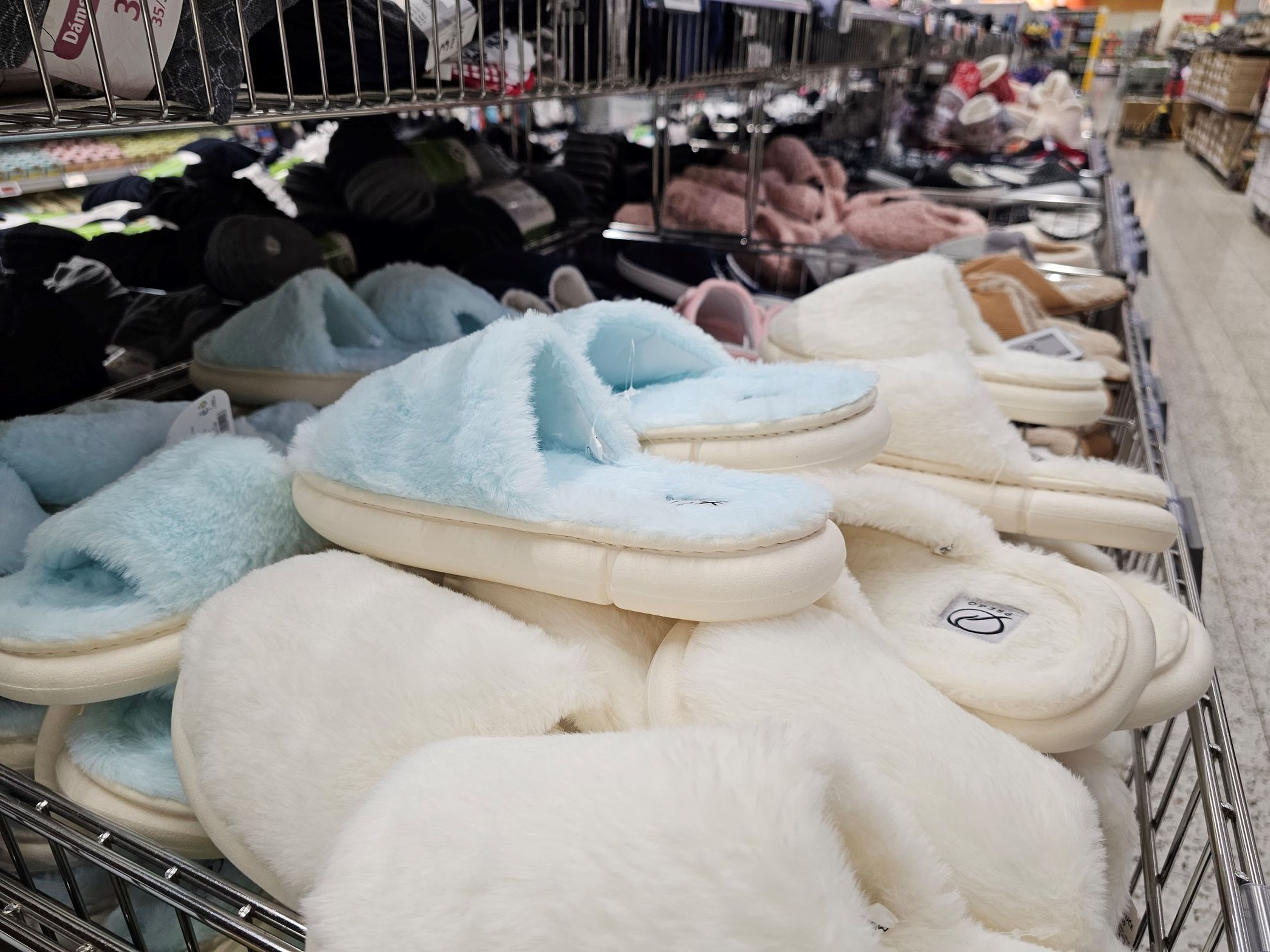 Regál v obchodě plný různých měkkých pantoflí v pastelových barvách, včetně modré a bílé, uspořádaných v úhledných řadách.