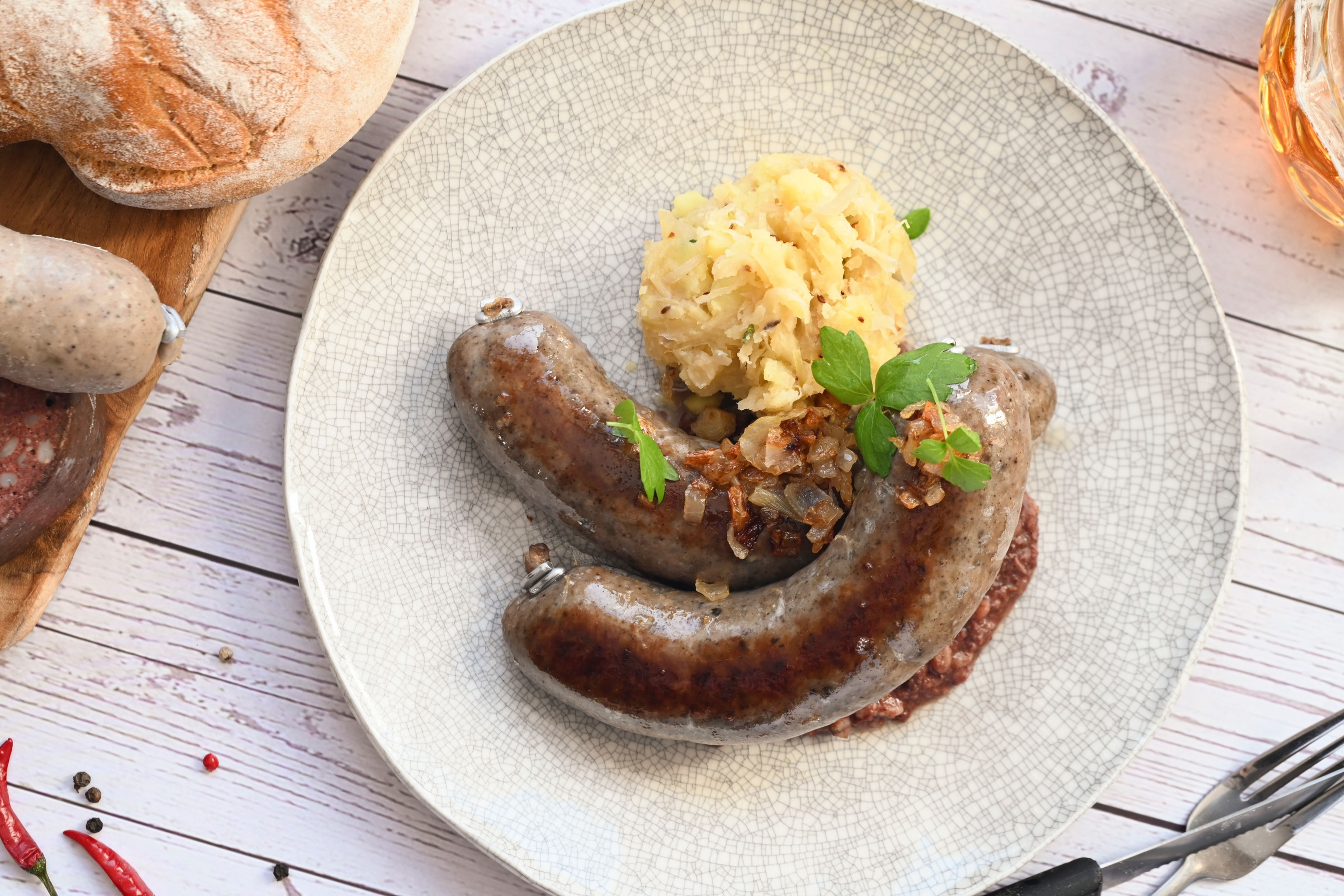 Talíř s jitrnicí s prejtem, bramborovou kaší a ozdobou. V pozadí chléb a pivo na dřevěném stole.