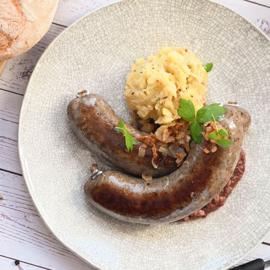 Talíř s jitrnicí s prejtem, bramborovou kaší a ozdobou. V pozadí chléb a pivo na dřevěném stole.