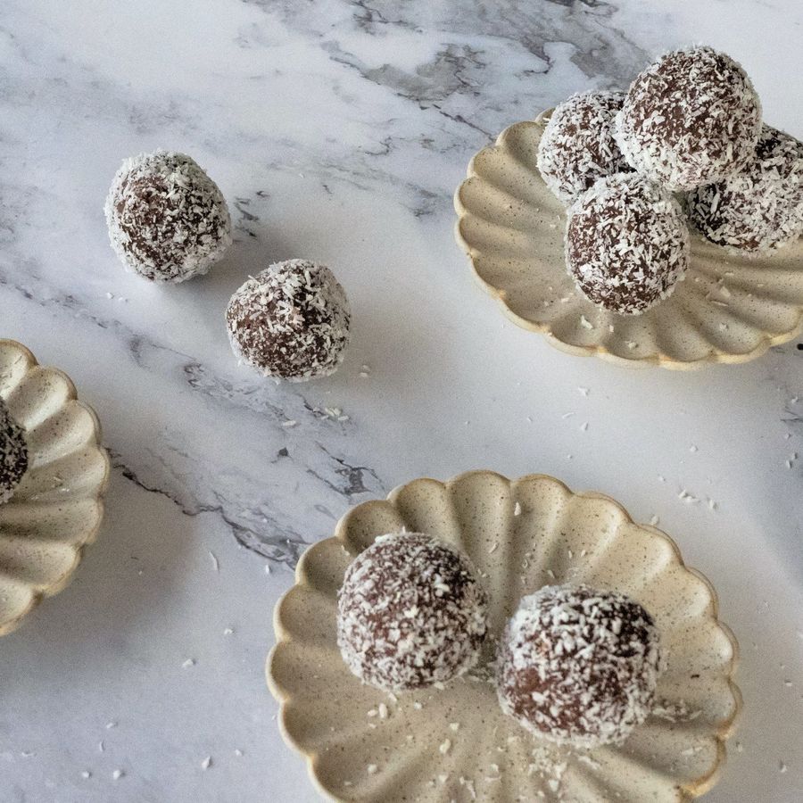 Rumové kuličky obalené kokosovými vločkami na vroubkovaných talířích, položené na mramorové desce.