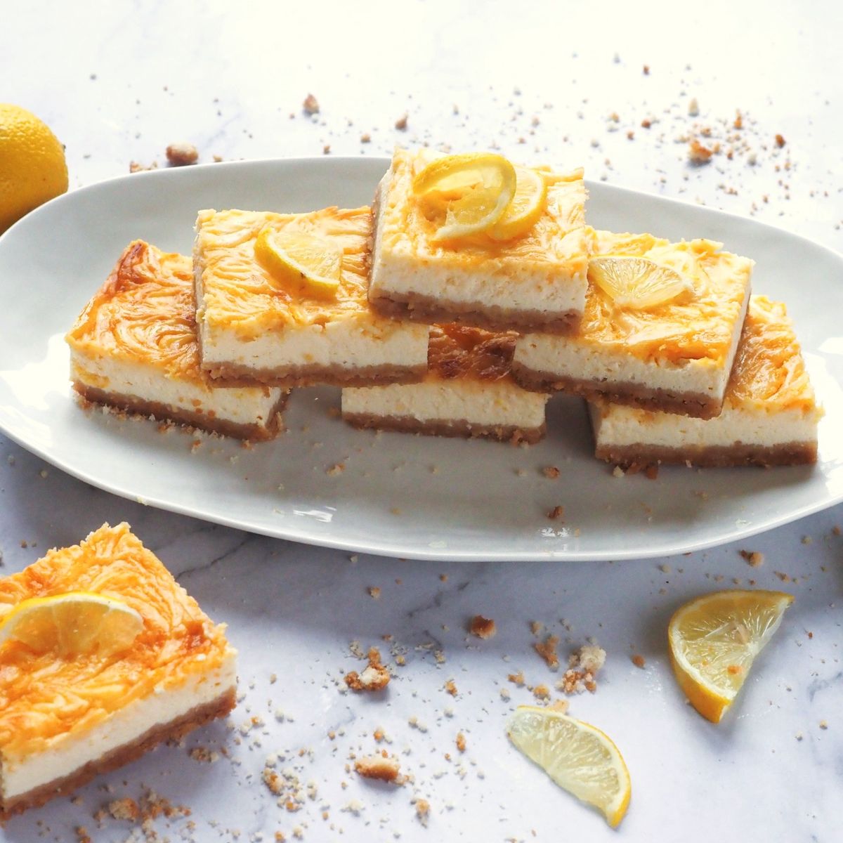 Lemon swirl řezy s krustou na bílém oválném talíři, zdobené plátky citronu a posypané drobky.