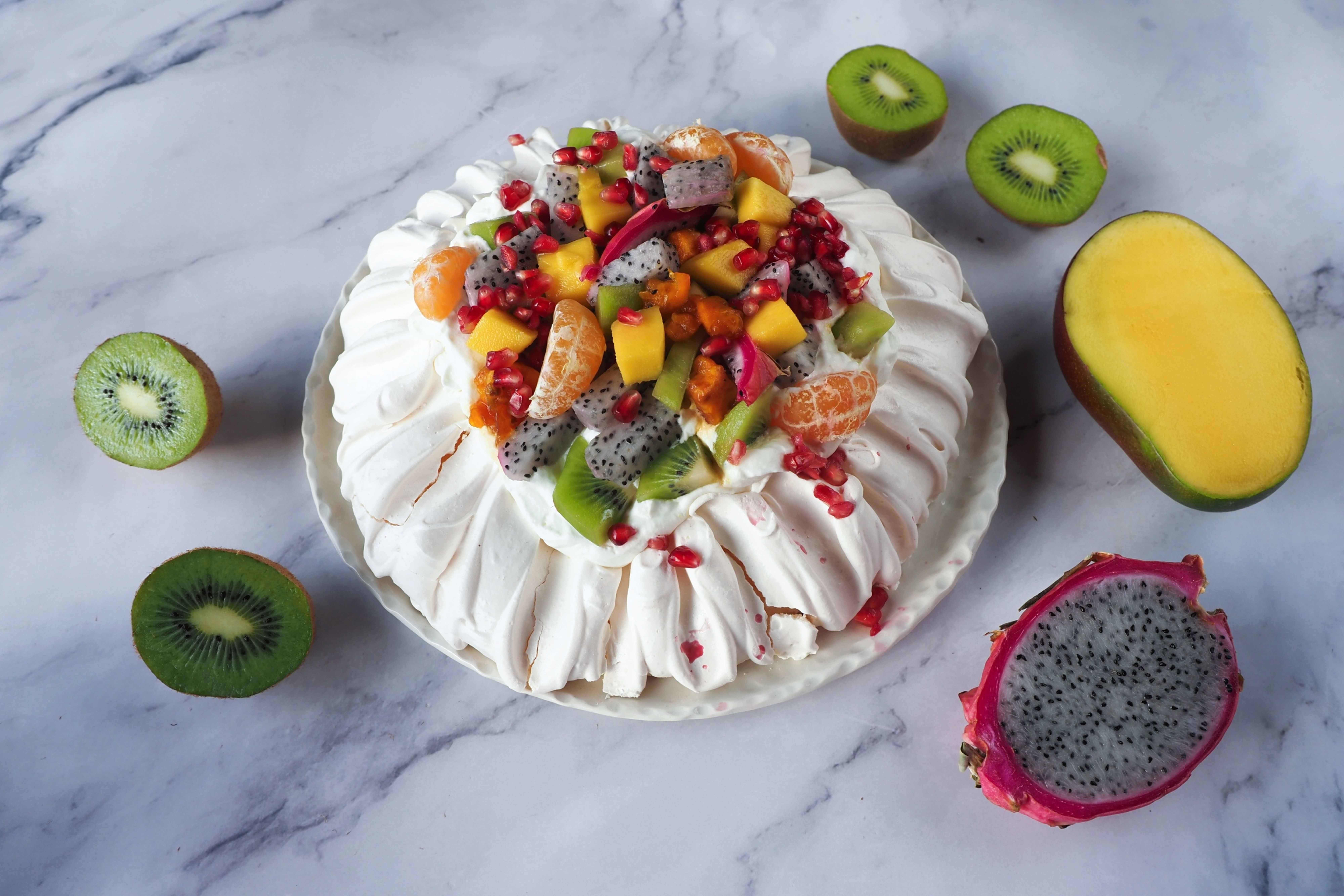 Pavlova s lehkým sněhovým korpusem a směsí ovoce – dračím ovocem, kiwi, mangem, granátovým jablkem a mandarinkami. Recept je z nabídky Globus.