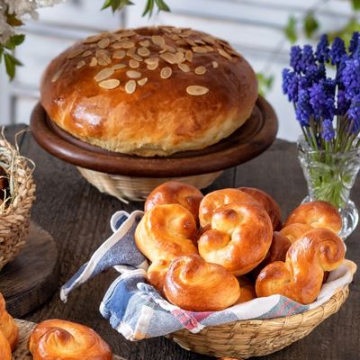 Stůl s mazancem posypaným mandlemi, košíkem zdobených vajec, čerstvě upečenými jidáši a květinami ve vázách.