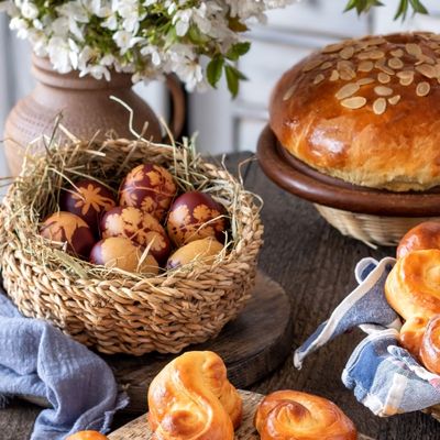 Stůl s mazancem posypaným mandlemi, košíkem zdobených vajec, čerstvě upečenými jidáši a květinami ve vázách.