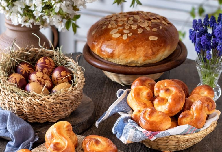 Stůl s mazancem posypaným mandlemi, košíkem zdobených vajec, čerstvě upečenými jidáši a květinami ve vázách.