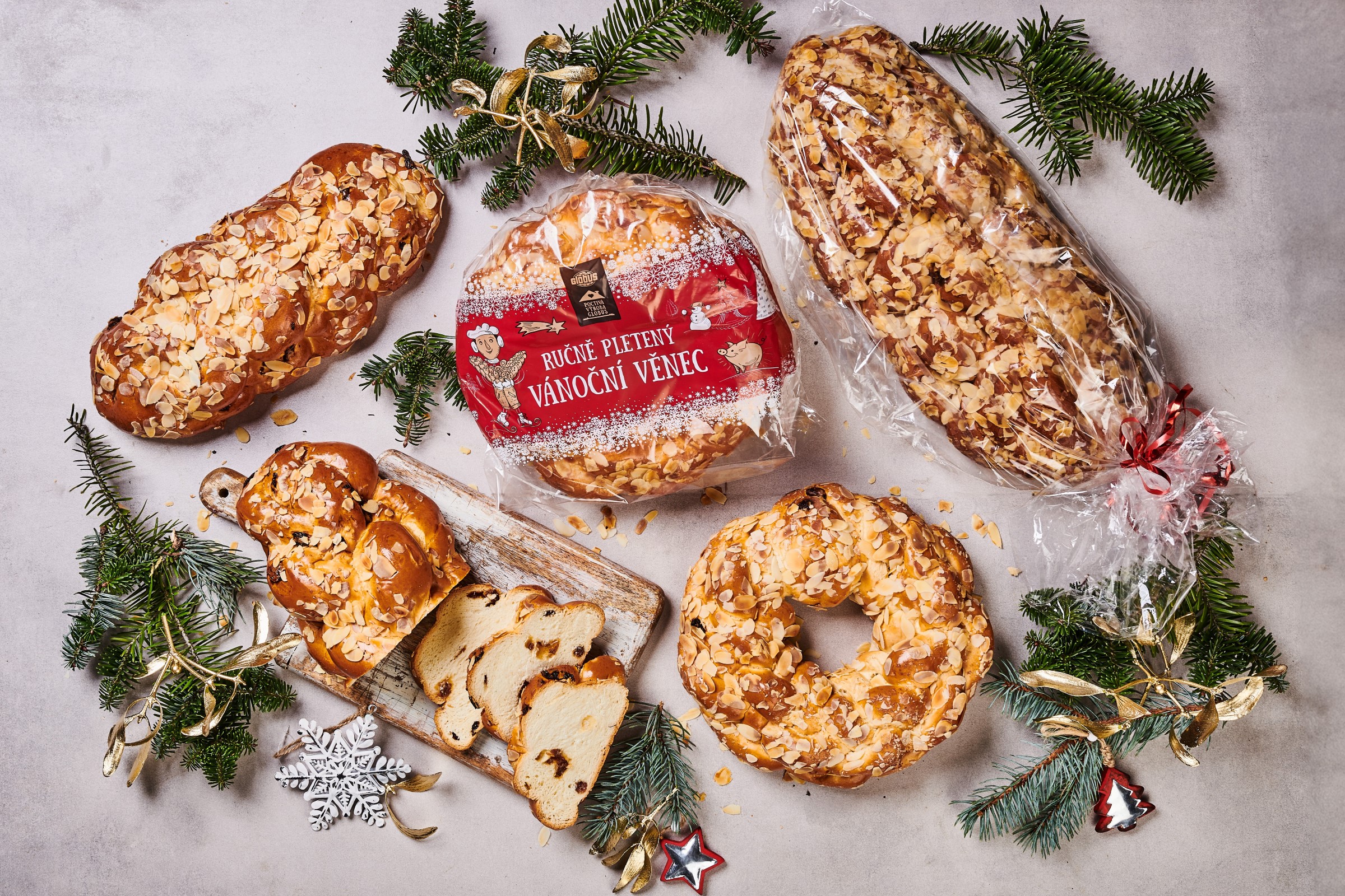 Různé druhy vánoček a vánočního věnce Globus s mandlemi, obklopené borovicovými větvičkami a ozdobami na světlém pozadí.