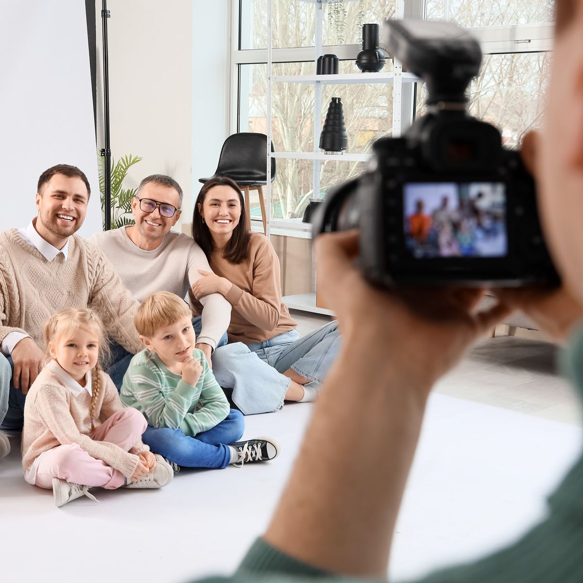 Šestičlenná rodinná skupina pózující pro focení, zachycená fotografem ve světlém prostředí ateliéru.