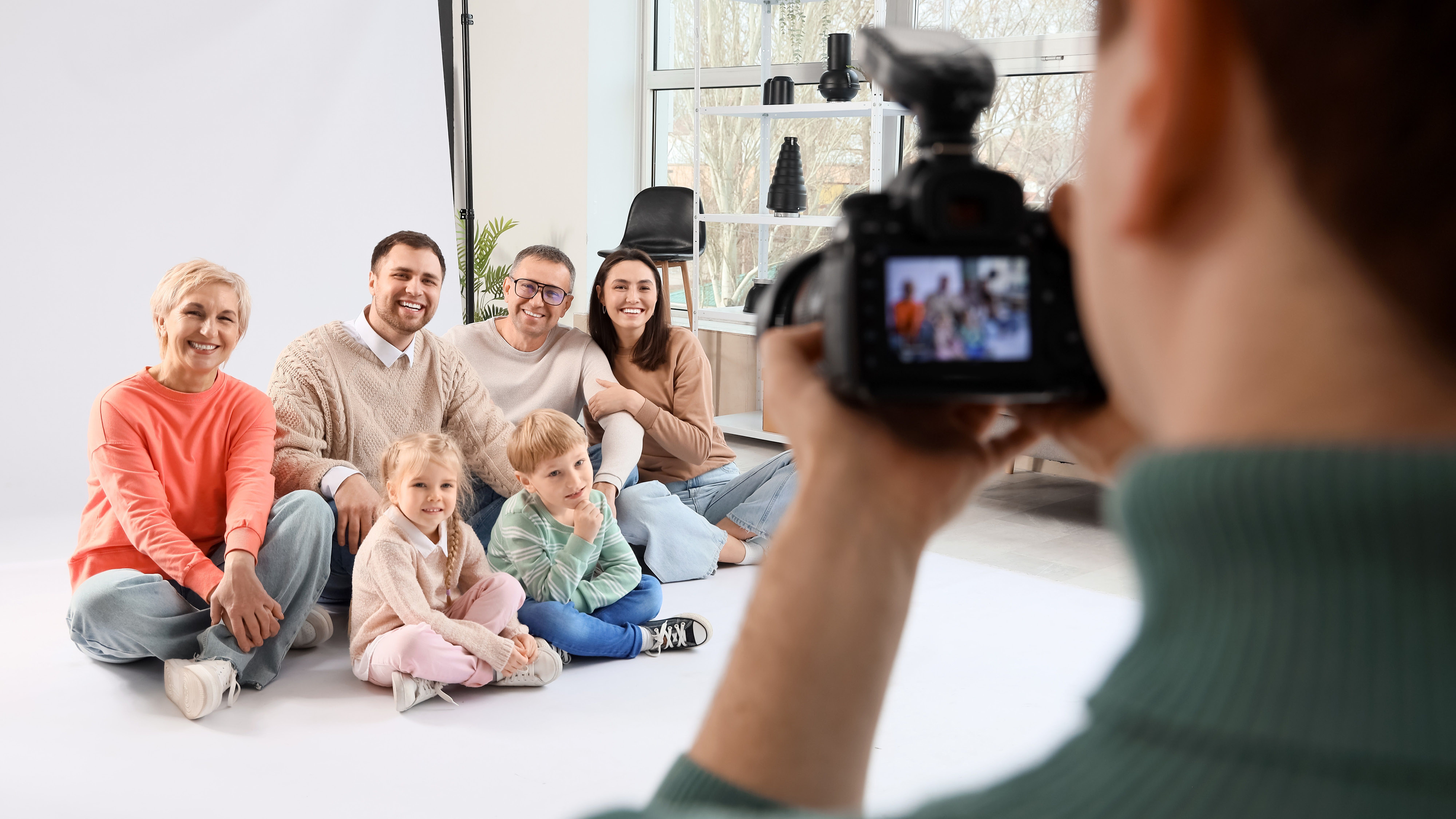 Šestičlenná rodinná skupina pózující pro focení, zachycená fotografem ve světlém prostředí ateliéru.