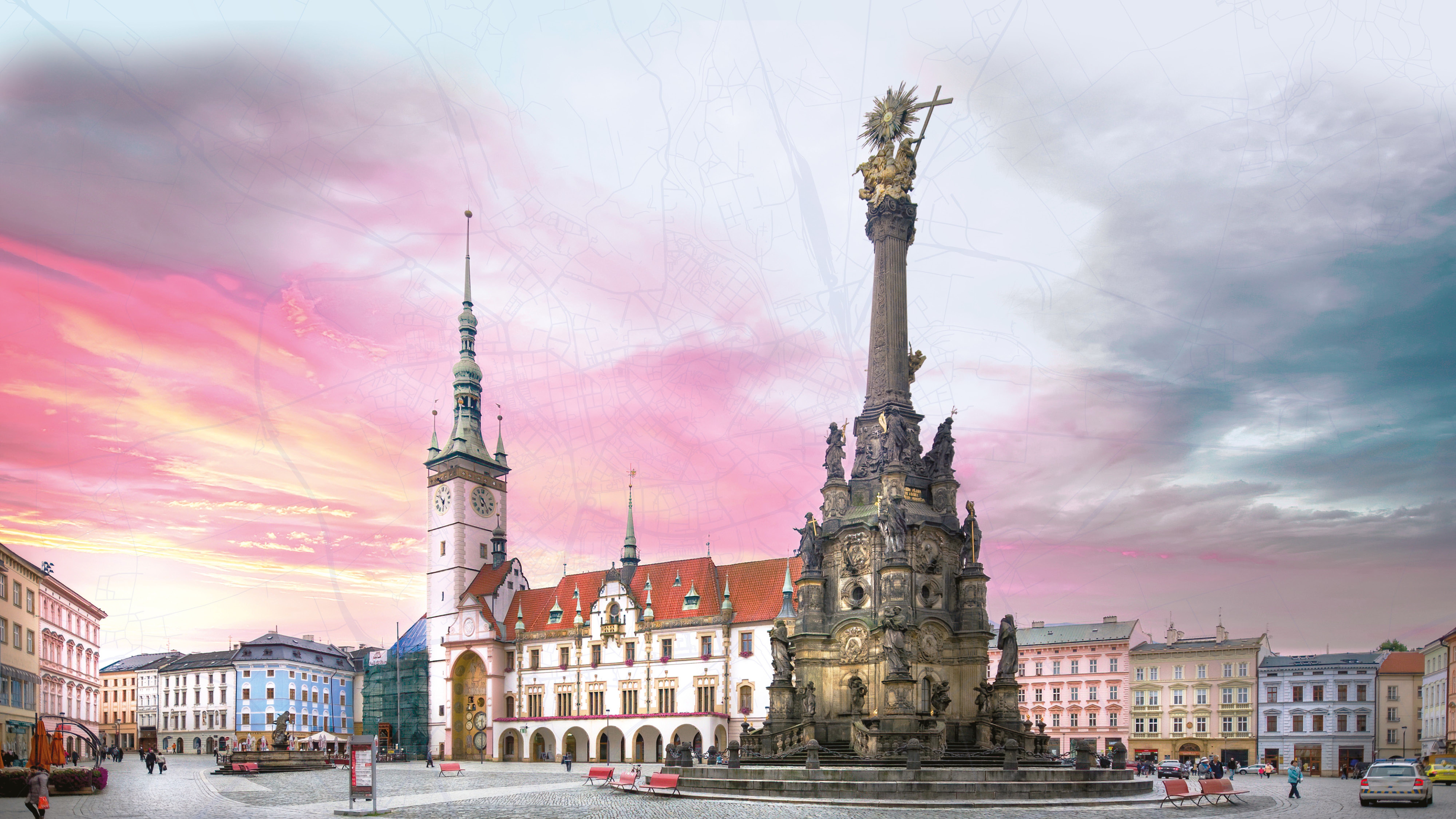 Historické náměstí se sloupem zakončeným sochou, obklopené barevnými budovami pod zářivě růžovo-modrou oblohou. Lidé procházejí po dlážděné ploše náměstí.