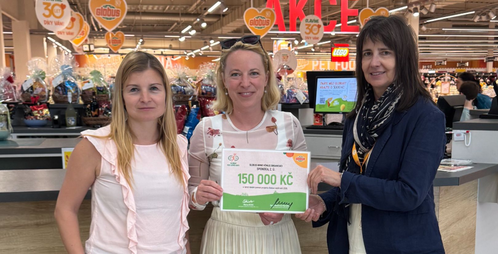 3 ženy v hypermarketu Globus s darovacím šekem na částku  150 000 Kč