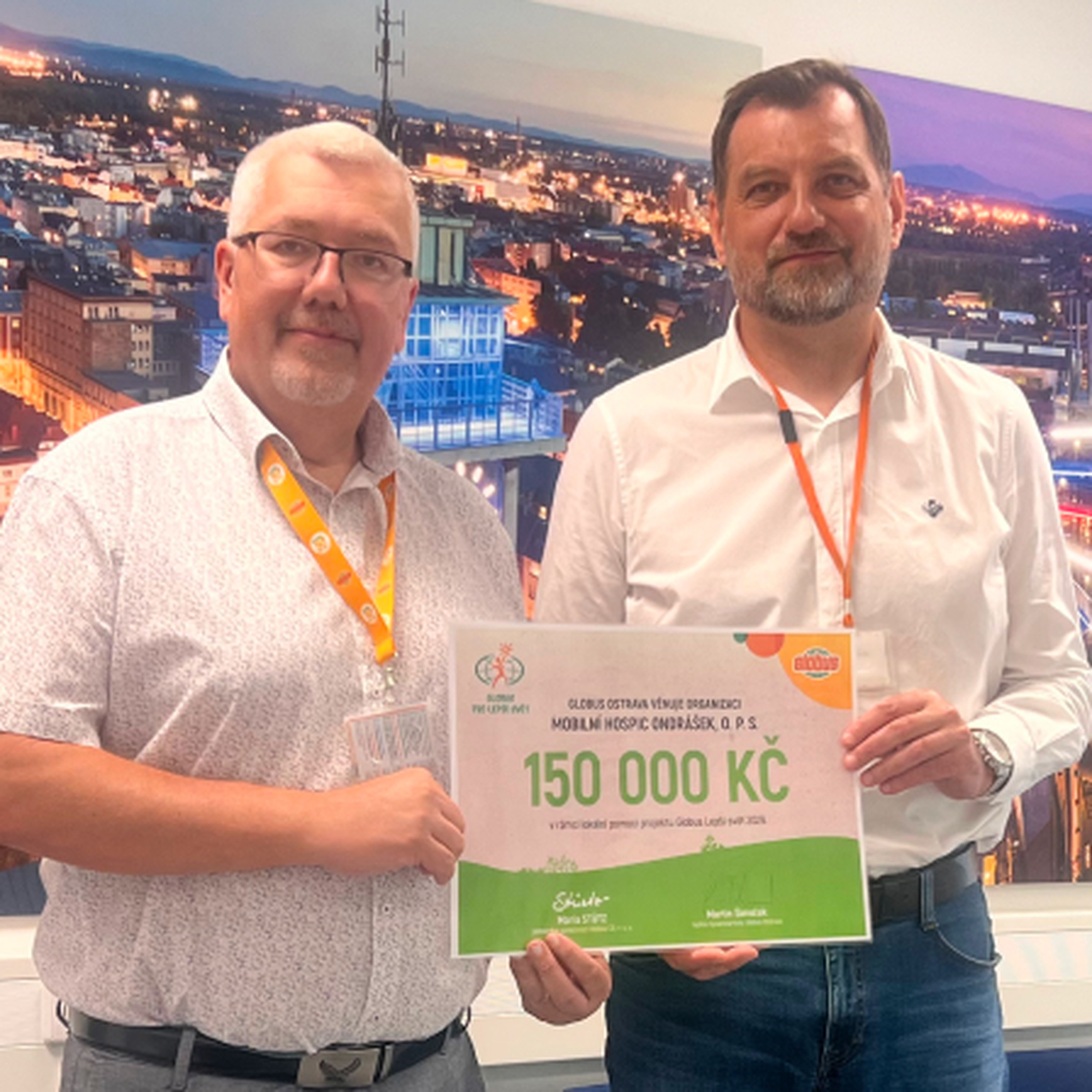 2 muži držící šek na 150 000 Kč před fotografií města