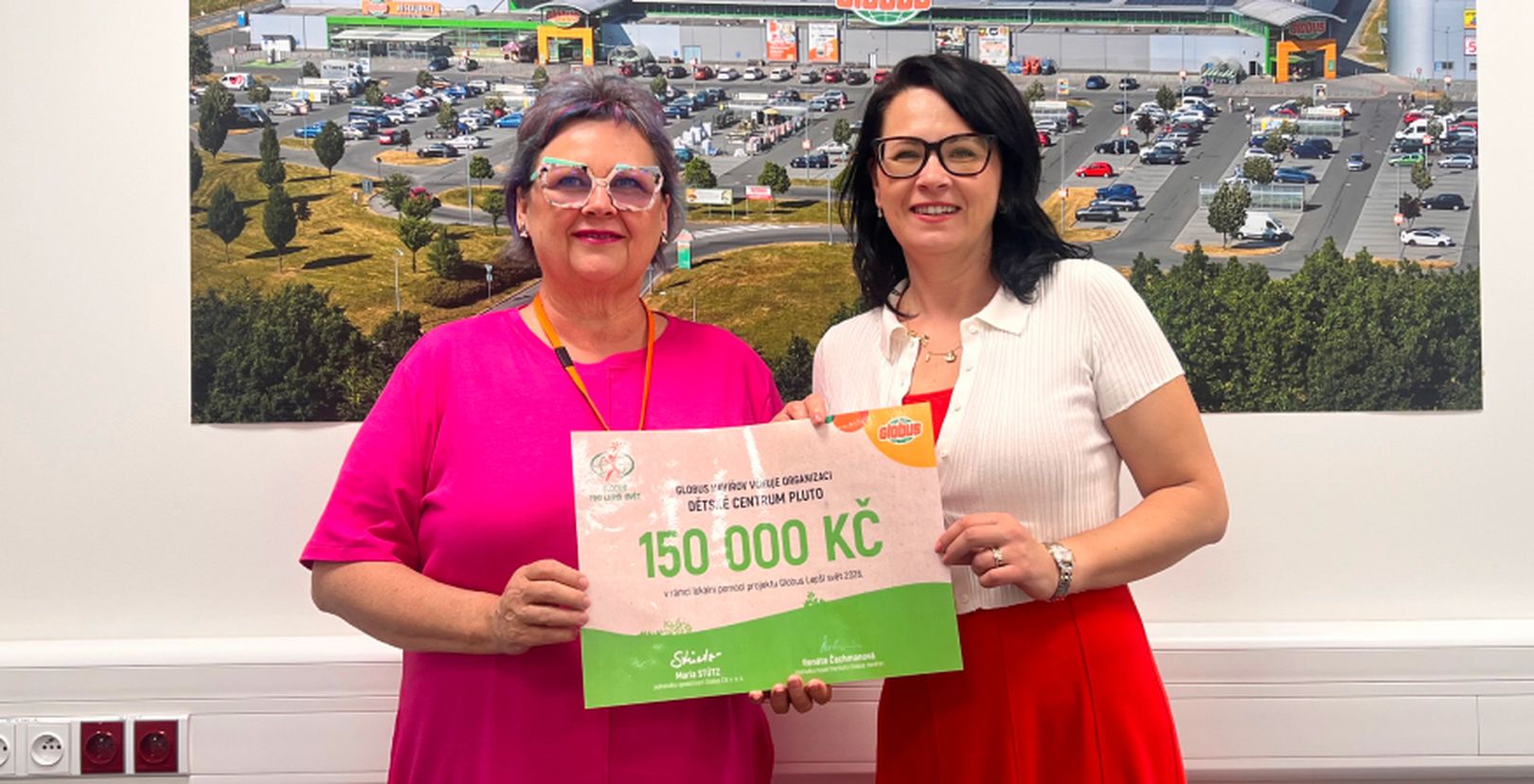 2 ženy před fotkou hypermarketu Globus s darovacím šekem na částku  150 000 Kč