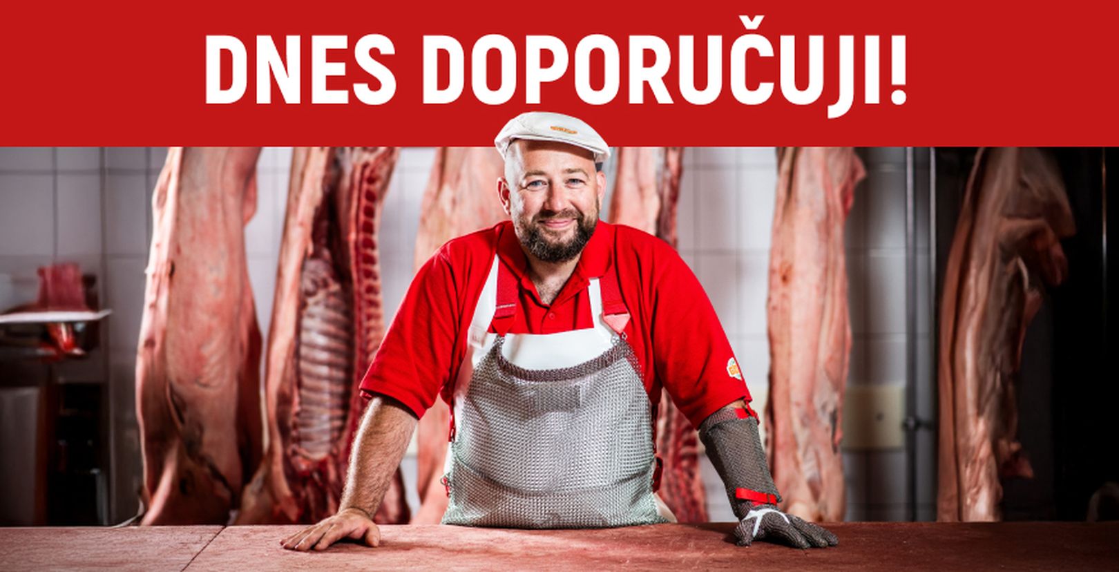Řezník v červené uniformě a kroužkové zástěře se opírá o pult, v pozadí visí maso. Nahoře je červený transparent s českým textem doporučuji.
