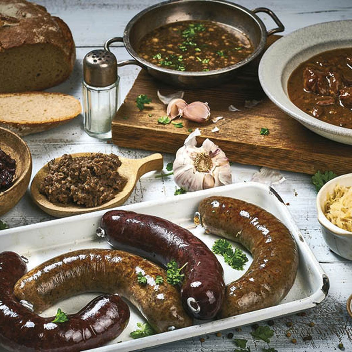 Rozmanité pokrmy na stole, včetně jaternic, jelit, dušeného masa, chleba, kysaného zelí a koření, cibule a česneku..