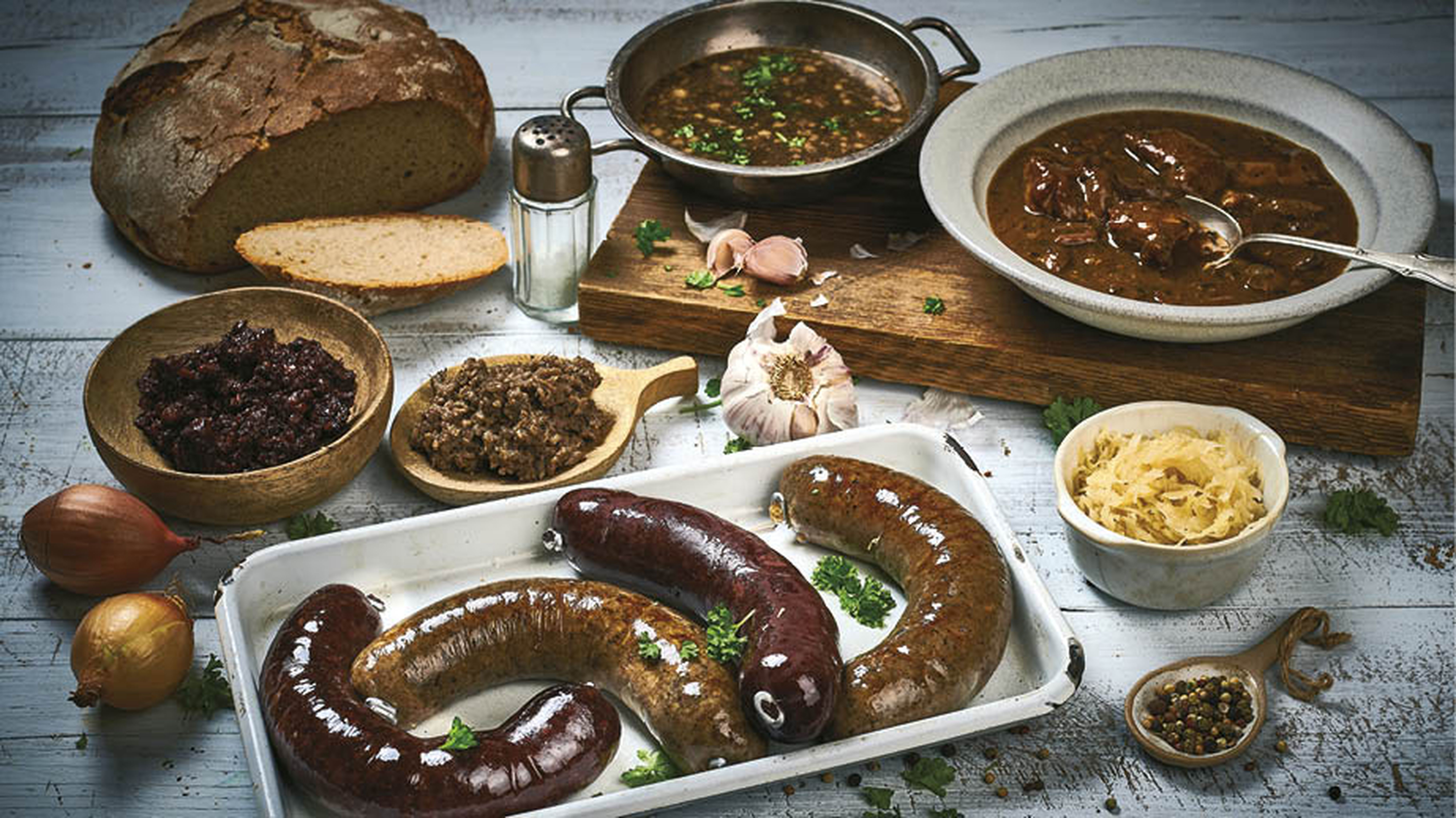 Rozmanité pokrmy na stole, včetně jaternic, jelit, dušeného masa, chleba, kysaného zelí a koření, cibule a česneku..