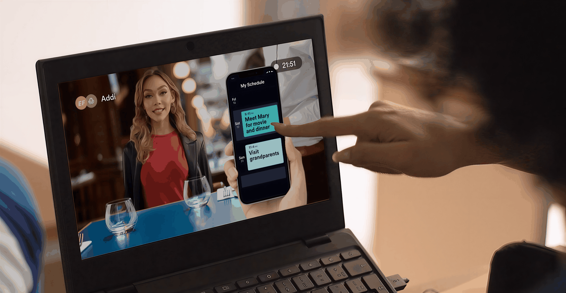 Person pointing at a smartphone screen in front of a laptop, displaying a video call with a woman.