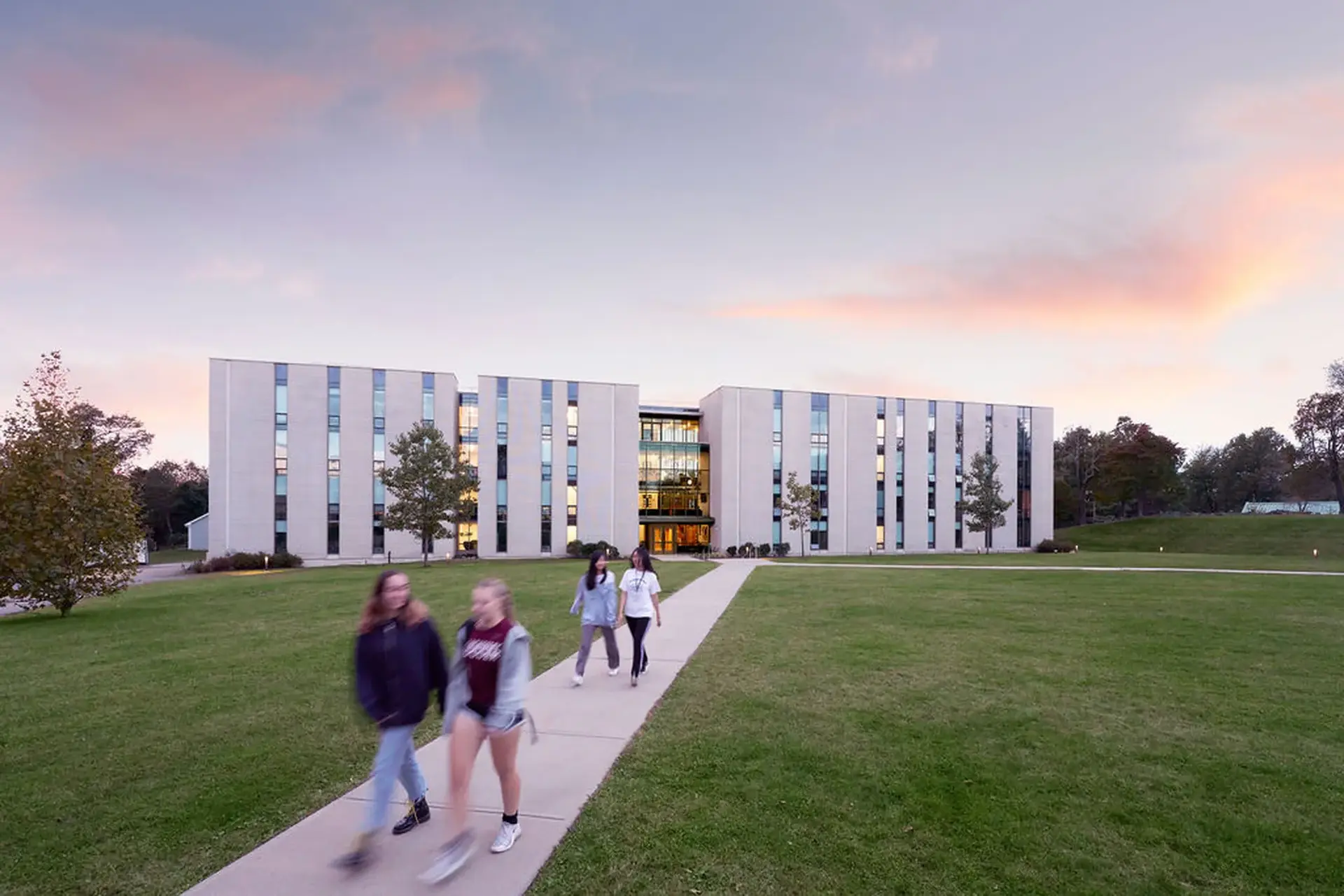 Students walking outside past the green lawn with the setting sun in the background