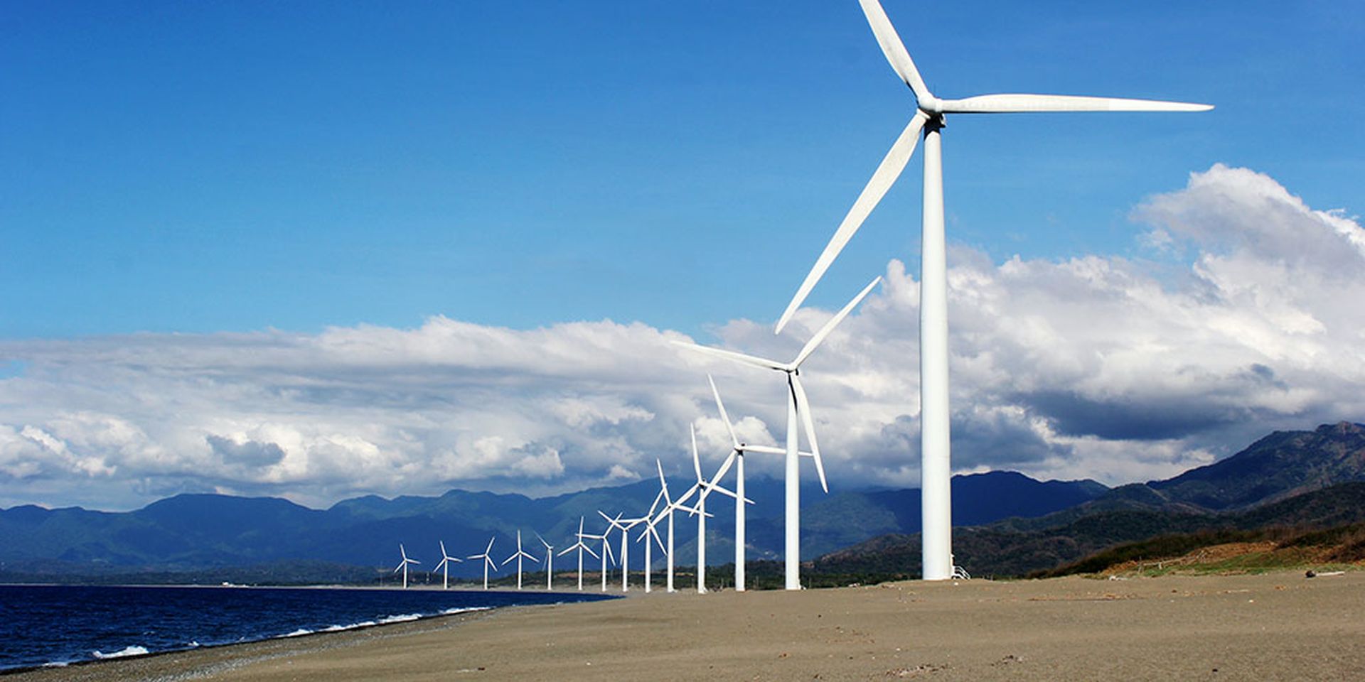 beeld van een rij windmolens aan de kustlijn met op de achtergrond een bergketen