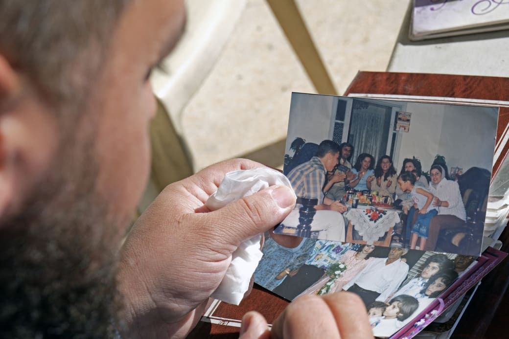 Person holding a tissue looks at a photo of a family gathering at a table, surrounded by photo albums.